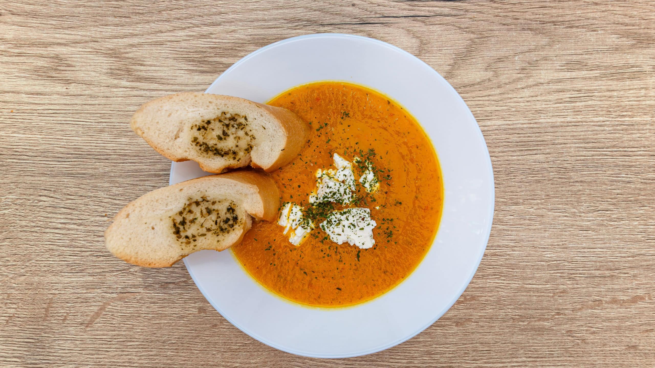 Polish pumpkin cream soup served with garlic bread slices and cheese on a wooden table