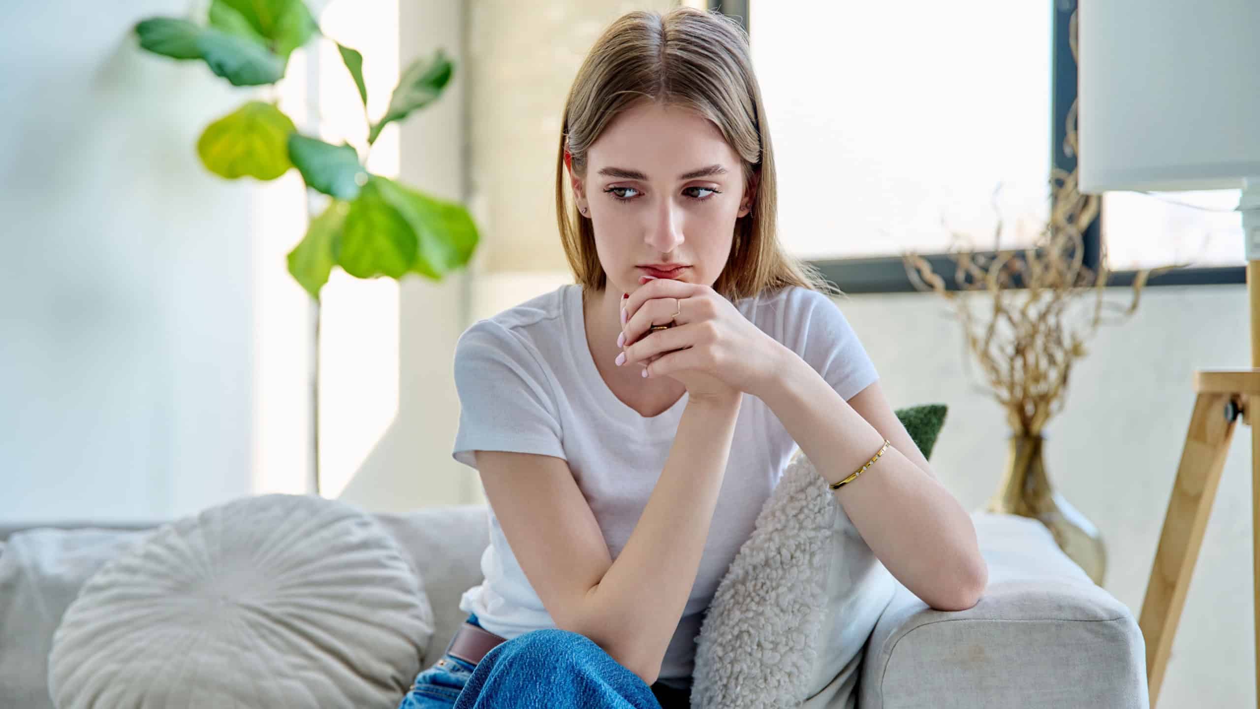 Sad unhappy stressed young woman sitting at home on sofa