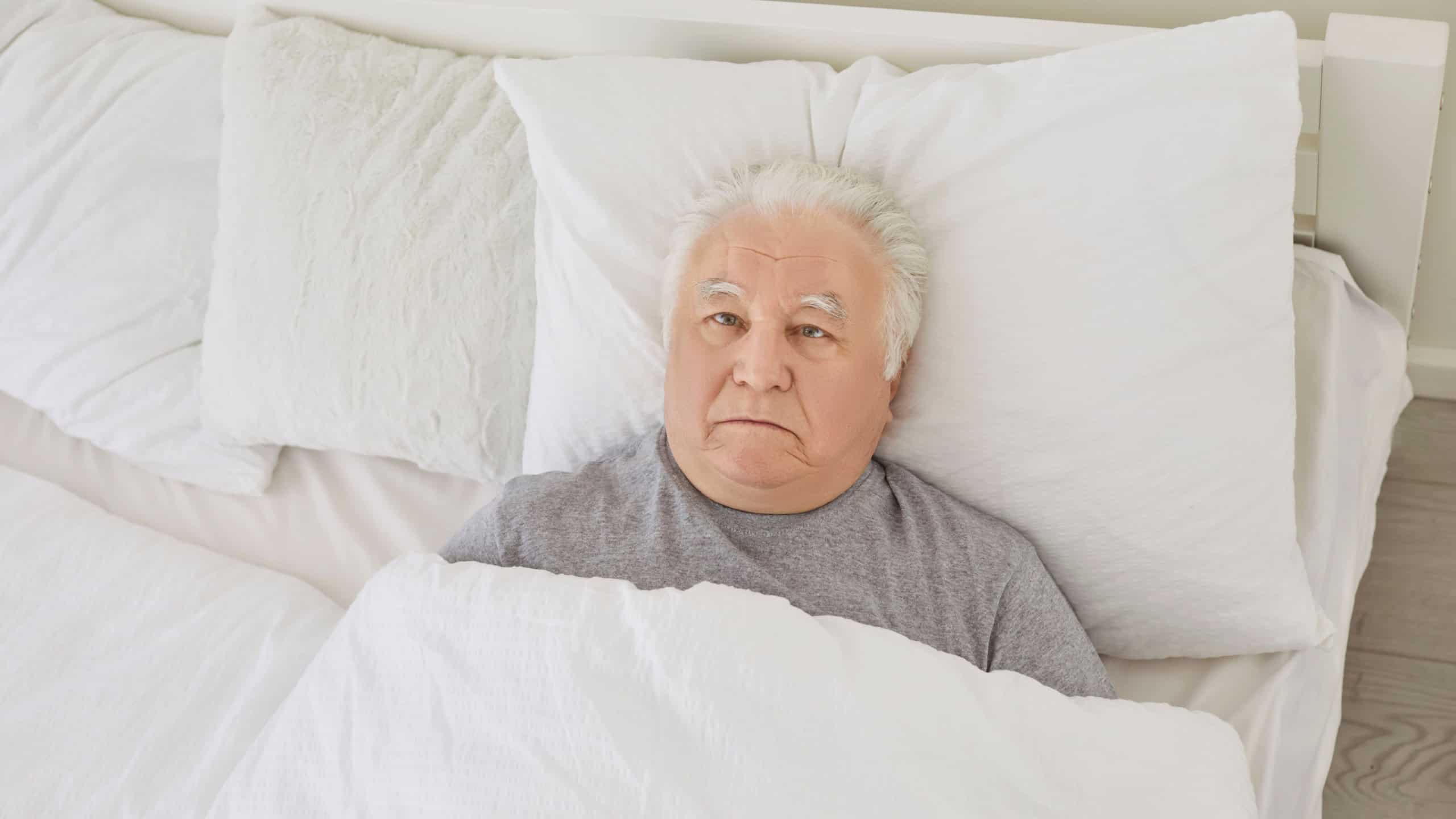 Senior man not sleeping. Unhappy old white haired man can't fall asleep lying awake in bed staring at ceiling with apathetic face expression late at night with light on. Insomnia sleeplessness concept