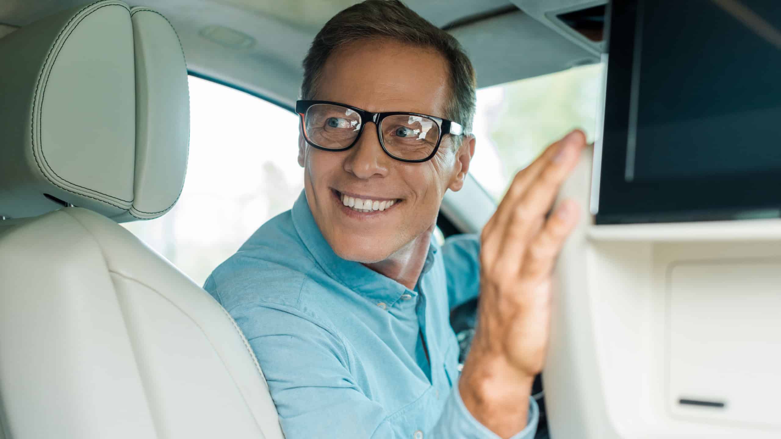 Smiling adult man driving luxury car and looking back