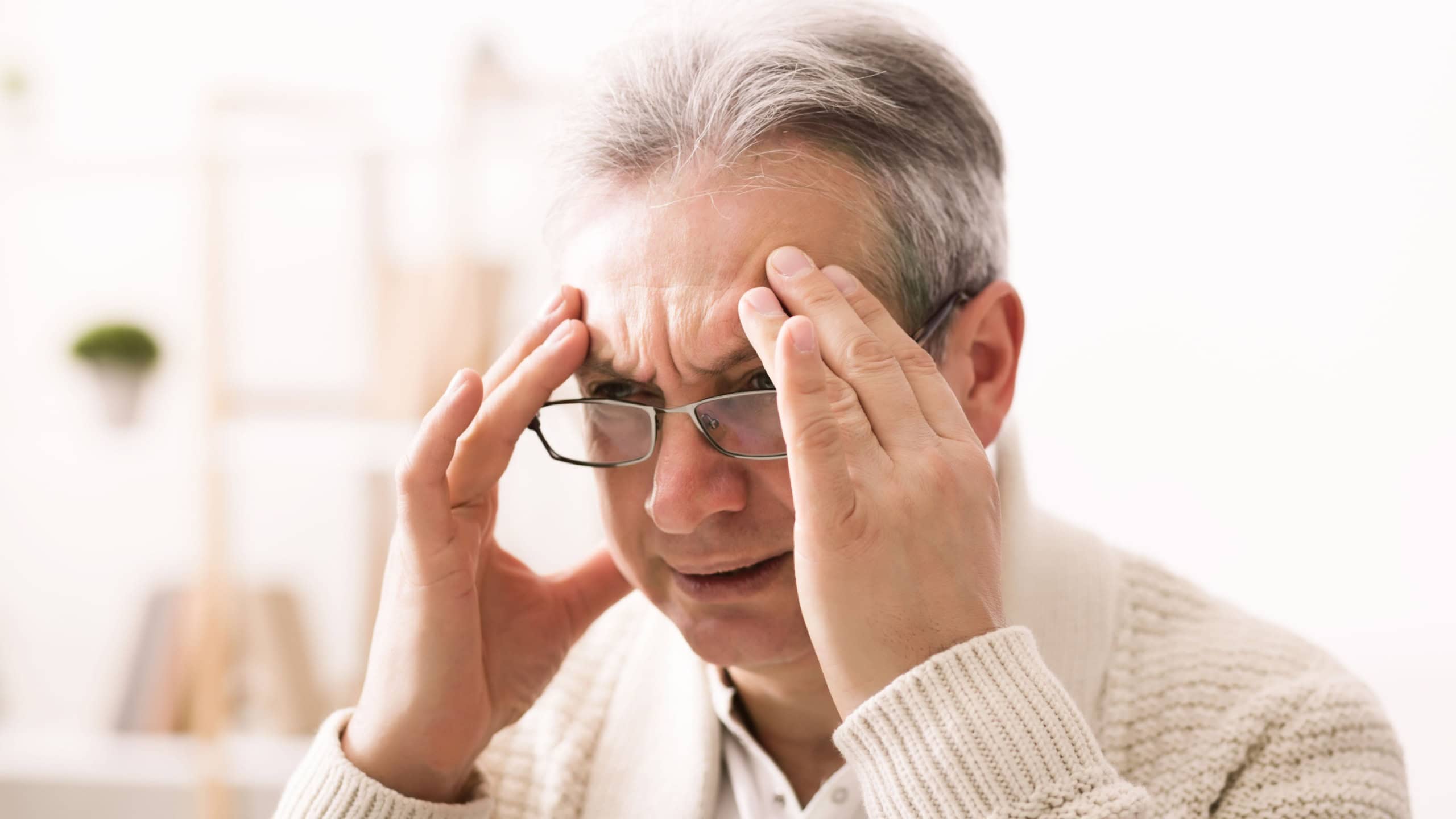 Horrible migraine. Sad senior man touching temples, sitting at home
