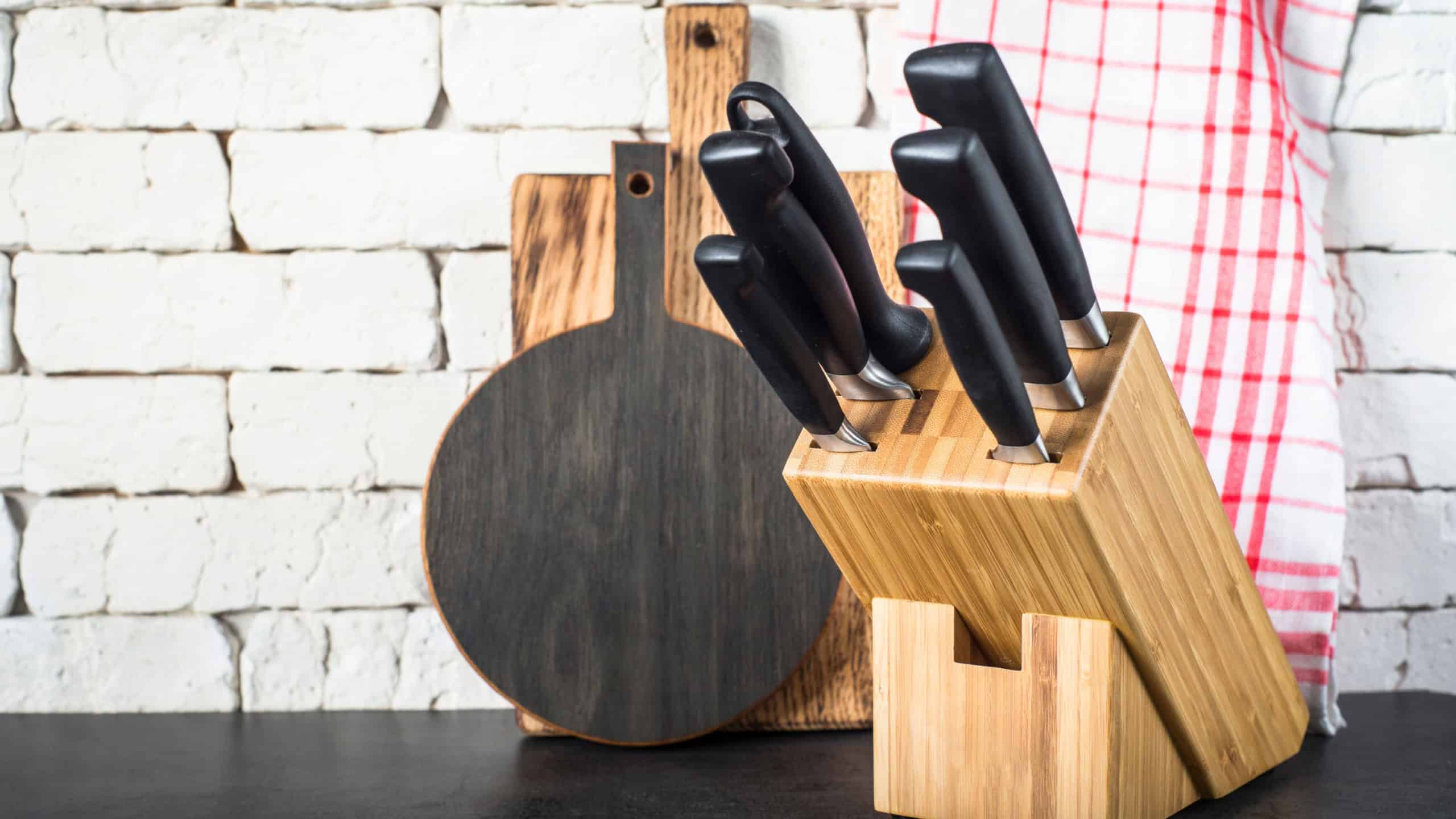 Kitchen knives set in the wooden block, cutting boards and towel on the kitchen black stone table near the brick wall.
