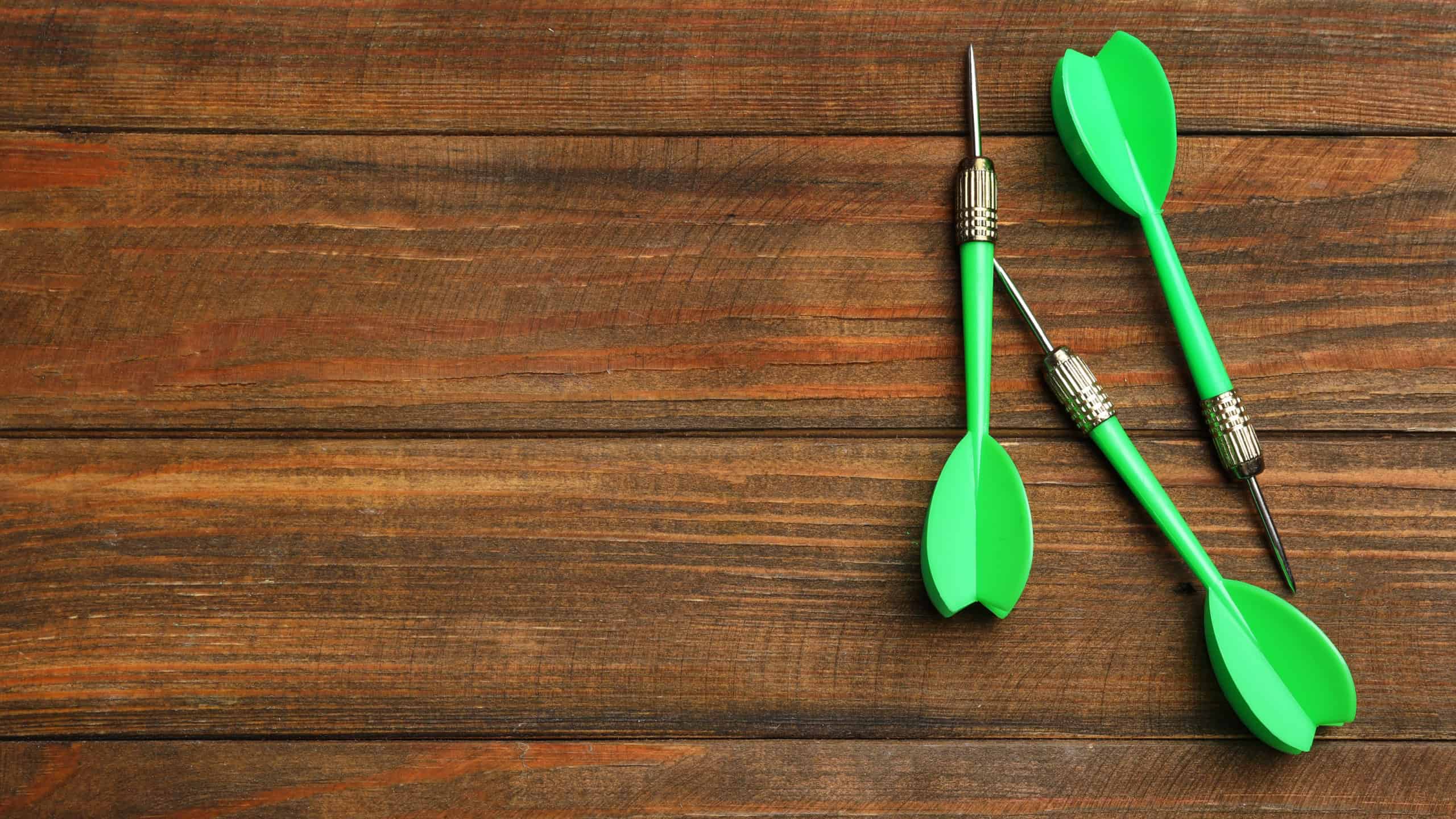 Dart arrows on wooden background, flat lay. Space for text
