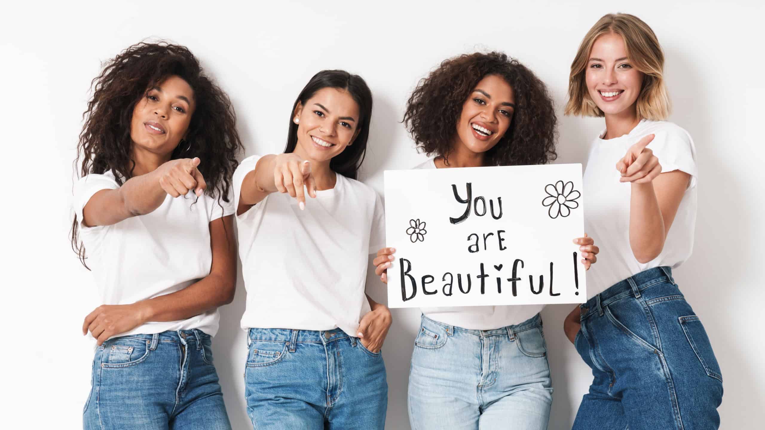 Image of a happy optimistic pleased young women multiracial friends posing isolated over white wall background holding blank with compliments text.