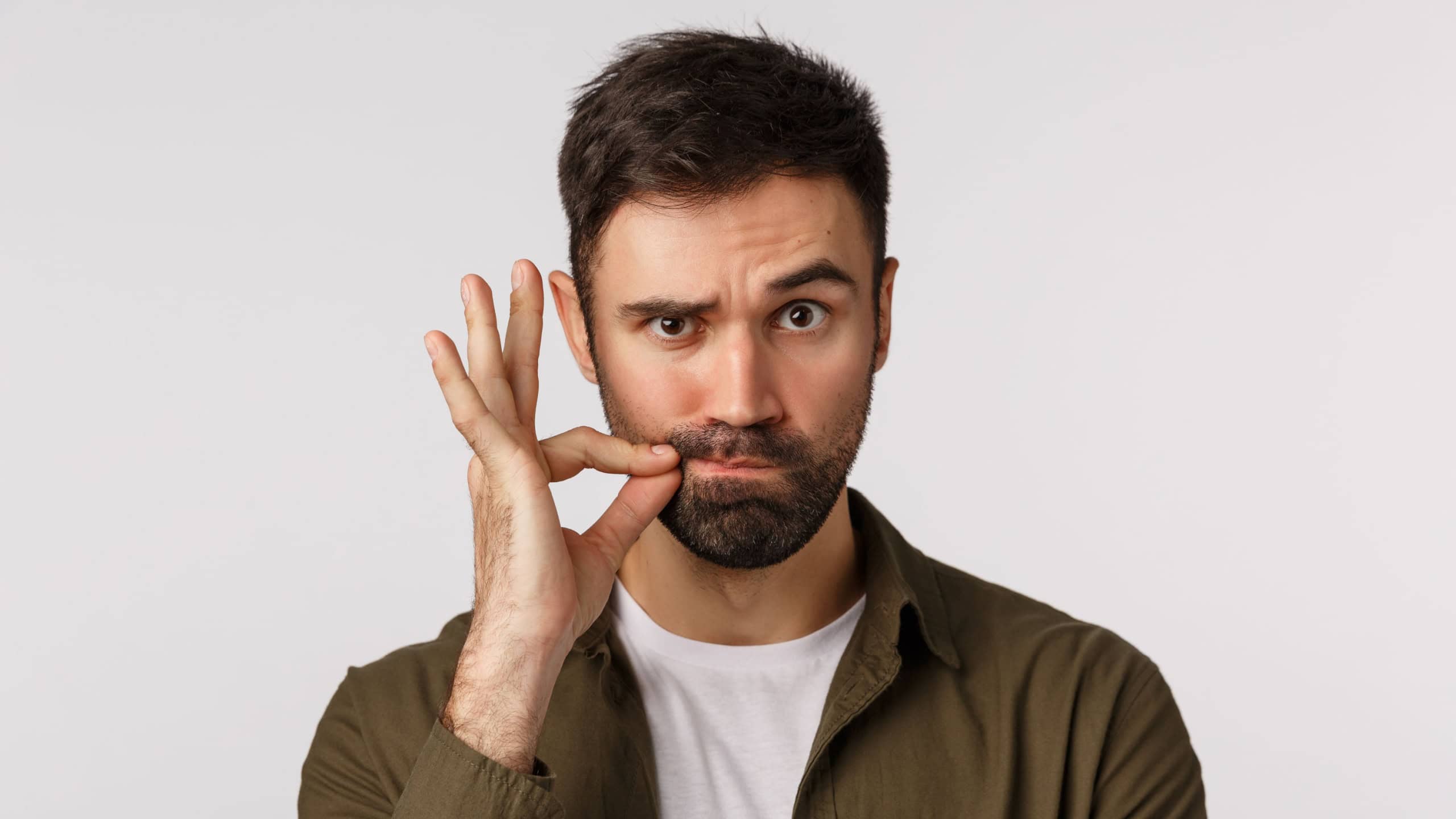 My lips are sealed with promise. Serious and funny bearded adult man keep mouth shut, making zip gesture and raise one eyebrow as hinting person stay silent, keep secret safe, white background