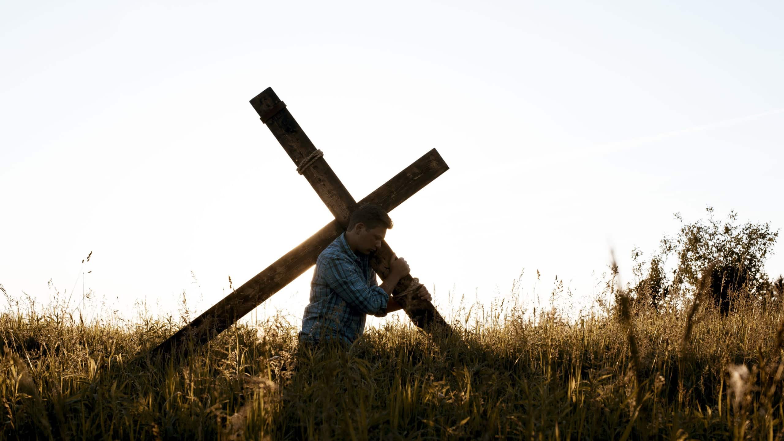 A male carrying a hand made a wooden cross through the dry grassy field