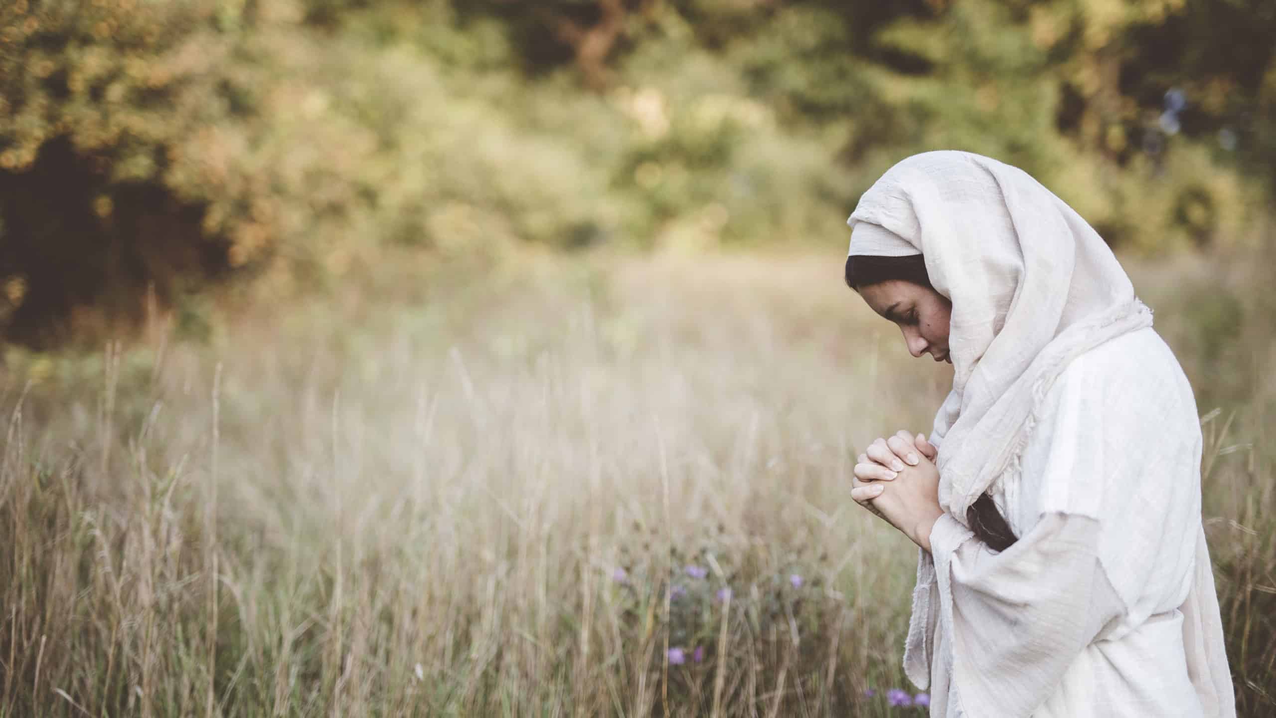 A shallow focus shot of a female wearing a biblical robe and praying while her eyes are closed