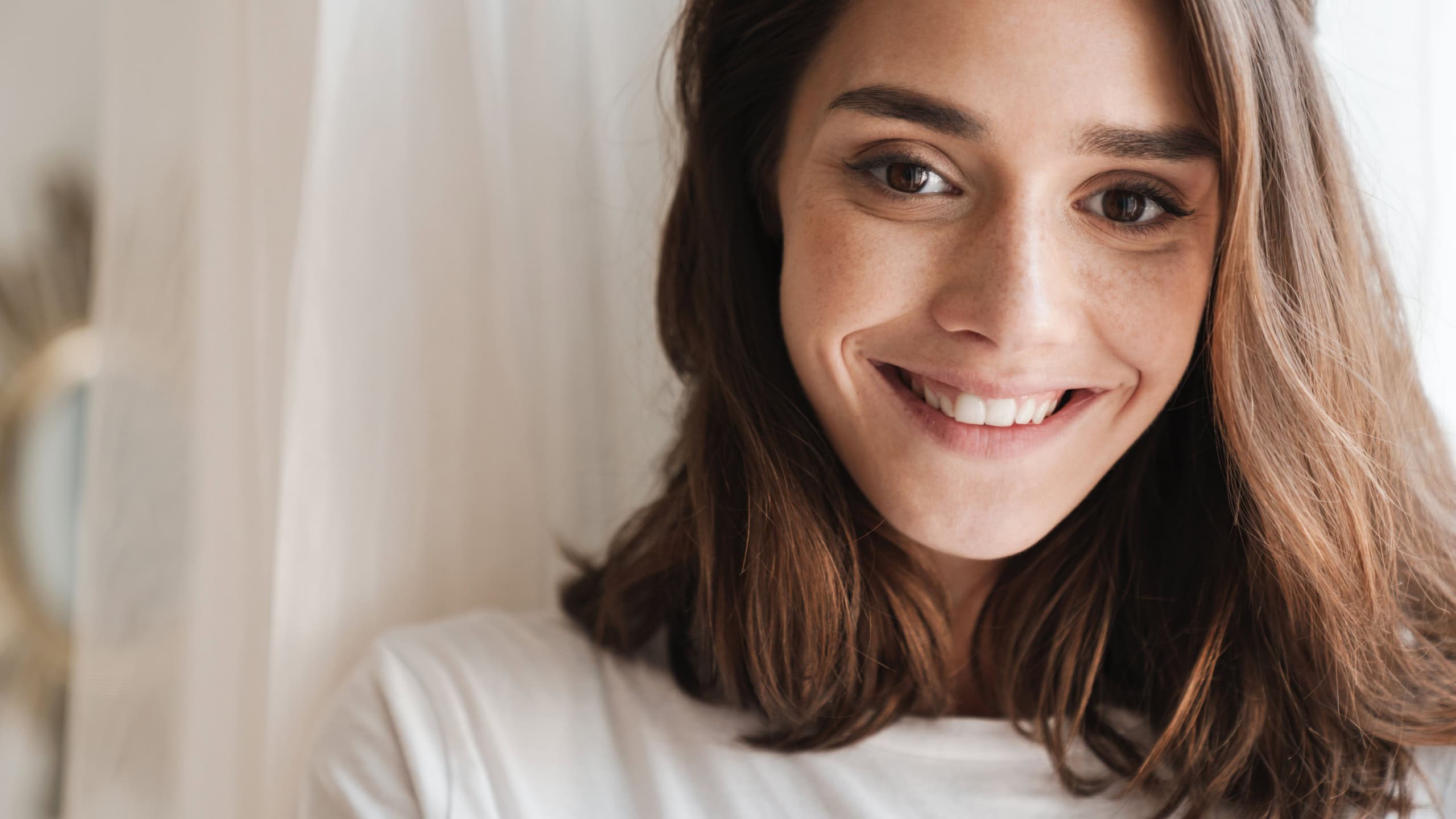 Picture of happy positive cheery young woman indoors at home posing near window.