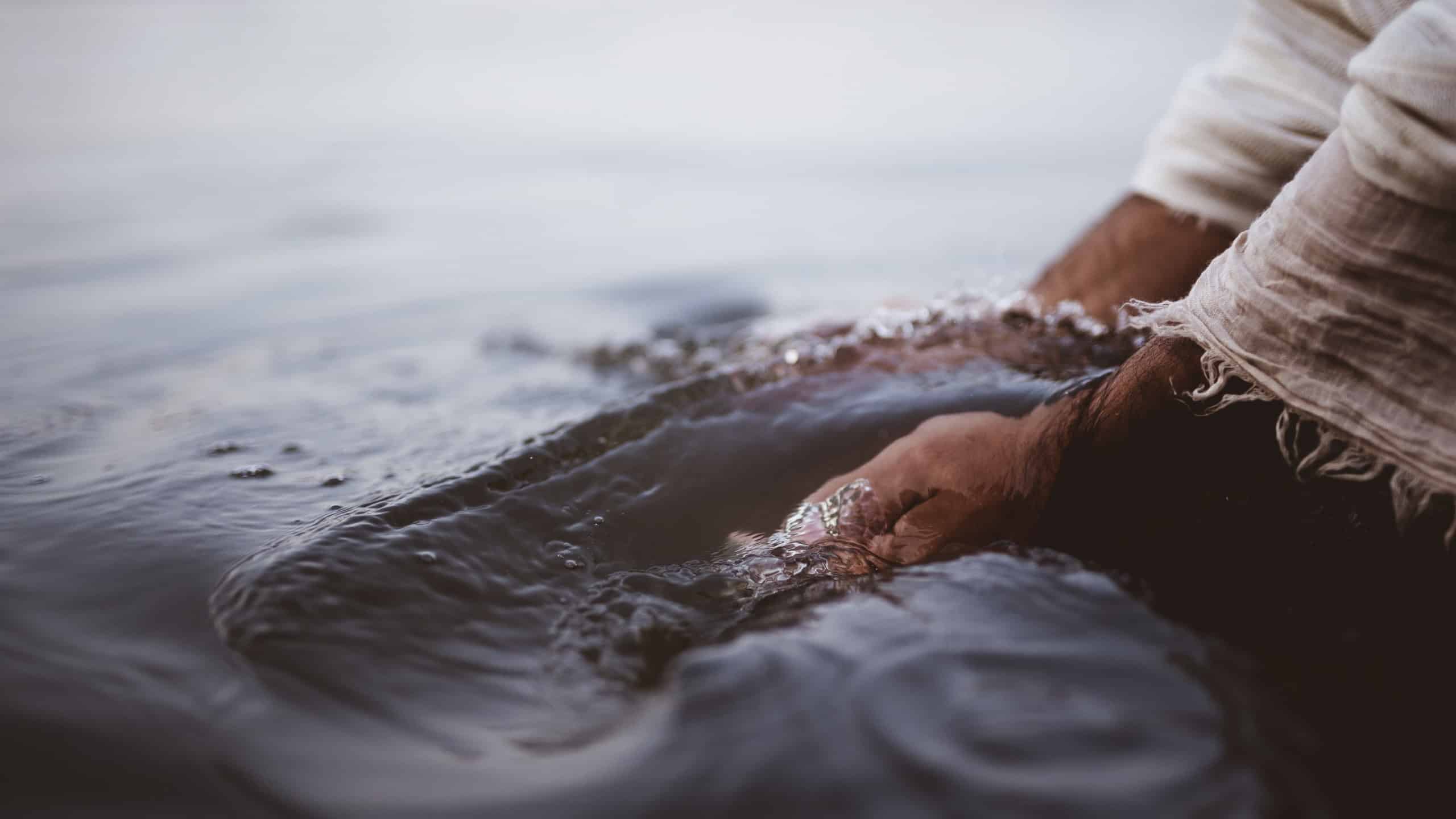 A closeup shot of a person wearing a biblical robe while washing his hands in the water