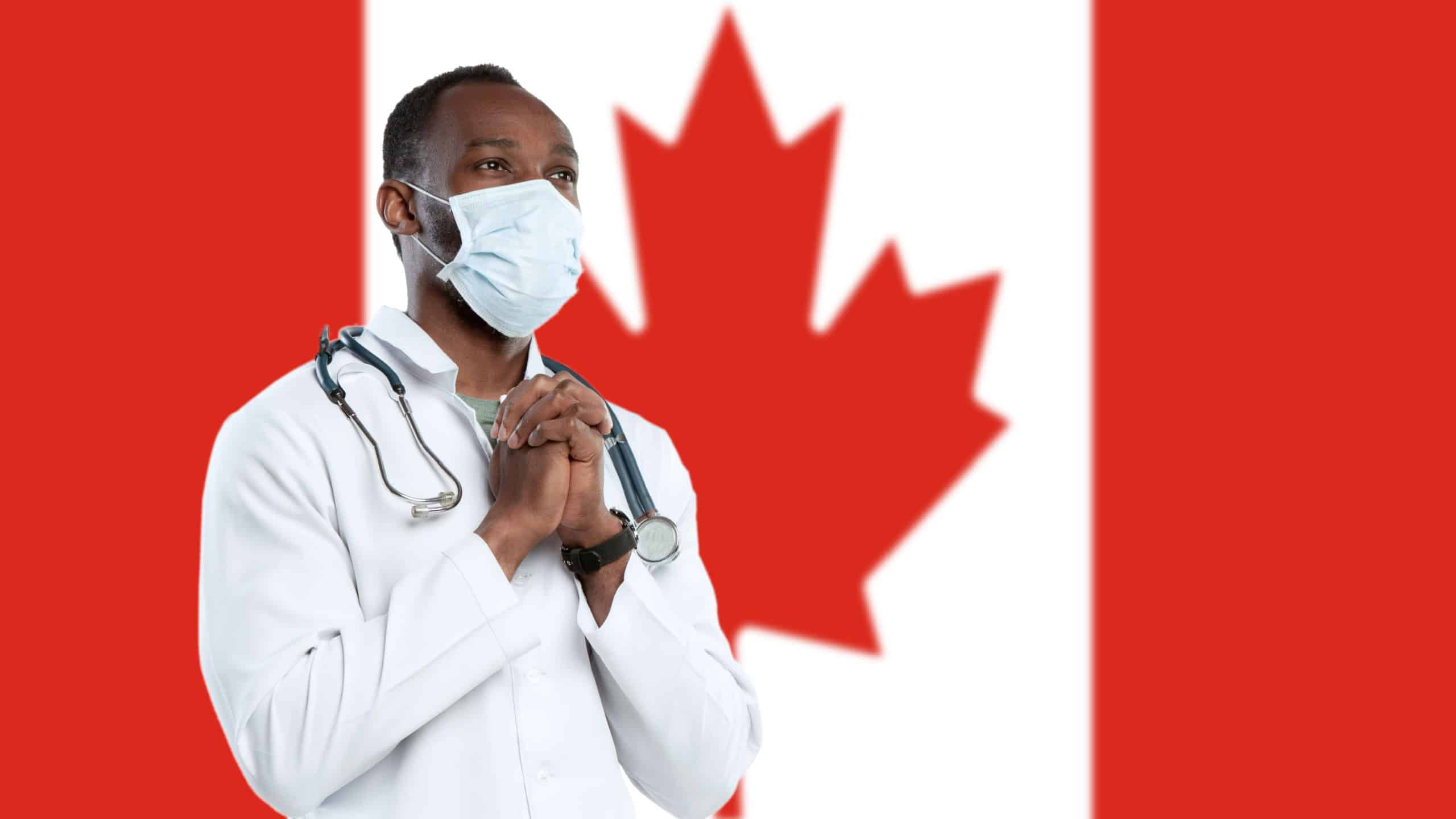 Young doctor with stethoscope and face mask praying for God with Canada national flag on background. Looks sad, serious. Concept of healthcare and medicine, coronavirus pandemic, danger epidemic