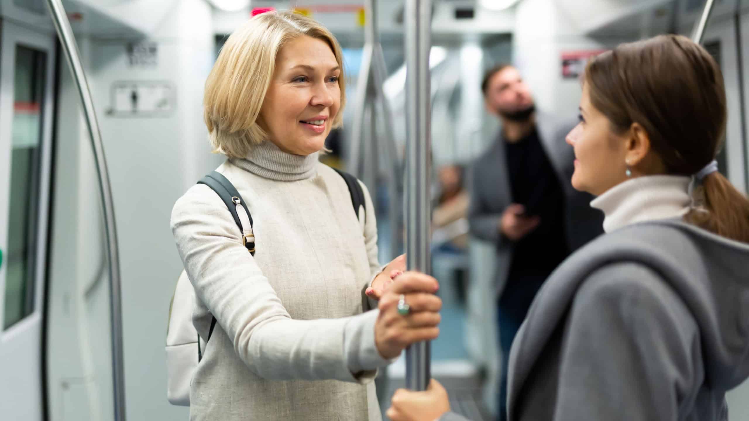 Portrait of mature woman talking friendly with her fellow traveler in modern subway car..