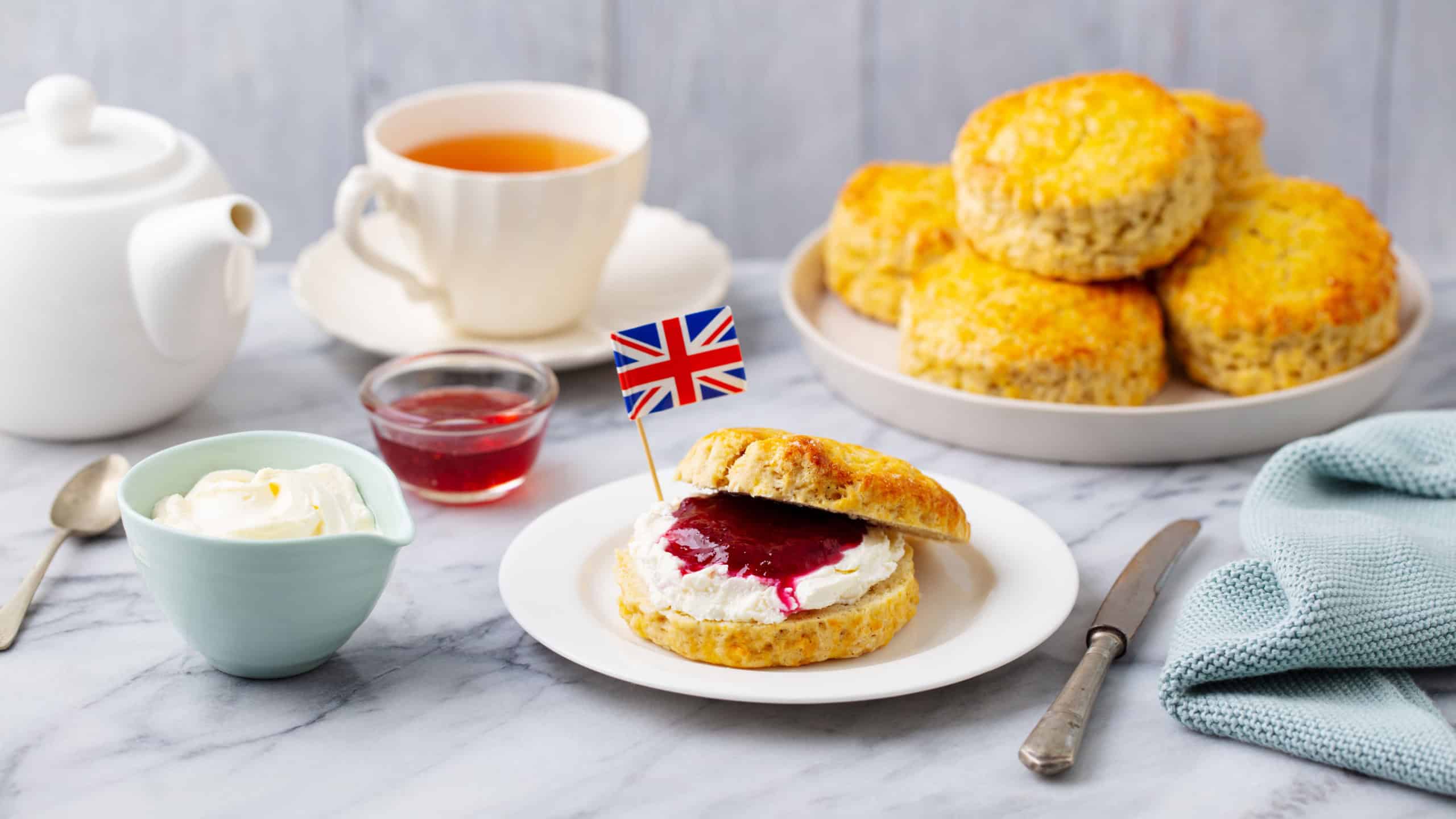 Scones, tea cakes with jam, clotted cream with the flag of Great Britain. Traditional British teatime. Grey background. Close up.