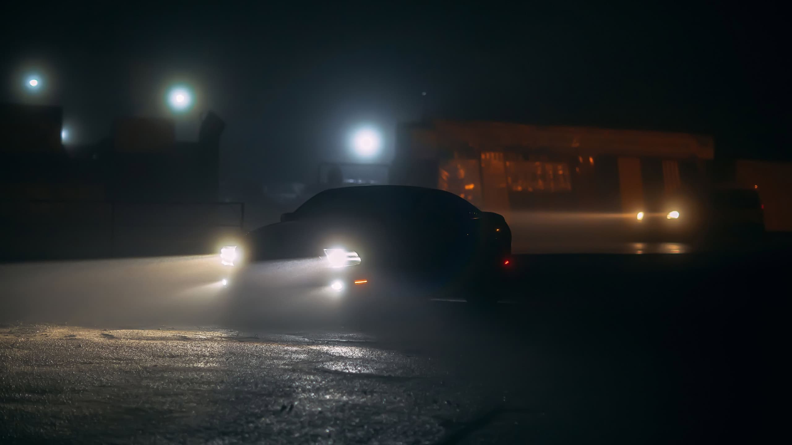 Sport car stands with in the shadows with glowing headlights at foggy night in low light, or silhouette of sport car dark background. Selective focus