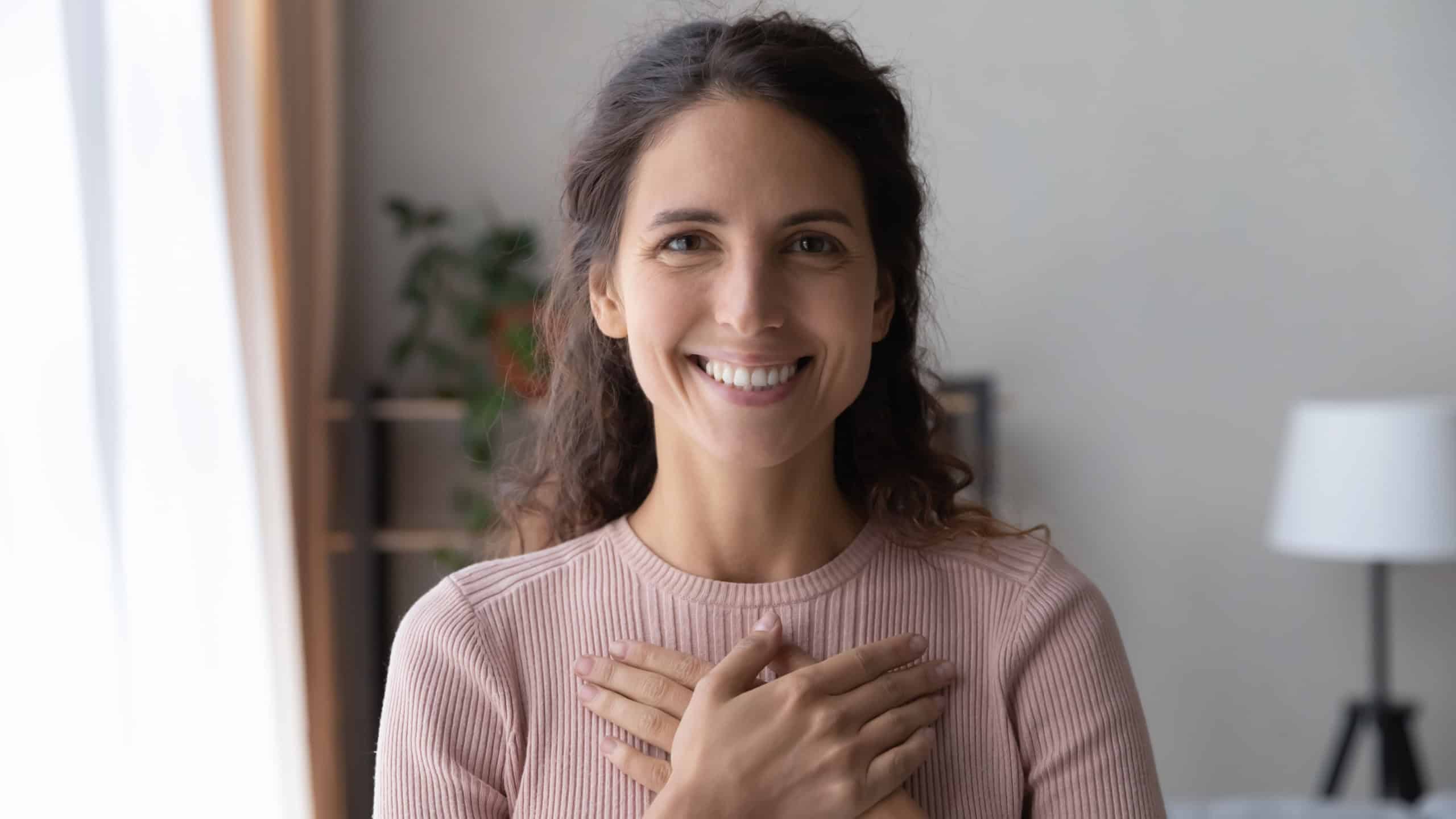 Portrait of happy millennial female volunteer holding folded hands on chest, looking at camera. Kind smiling young woman feeling thankful, showing appreciation, gratitude believe charity concept.