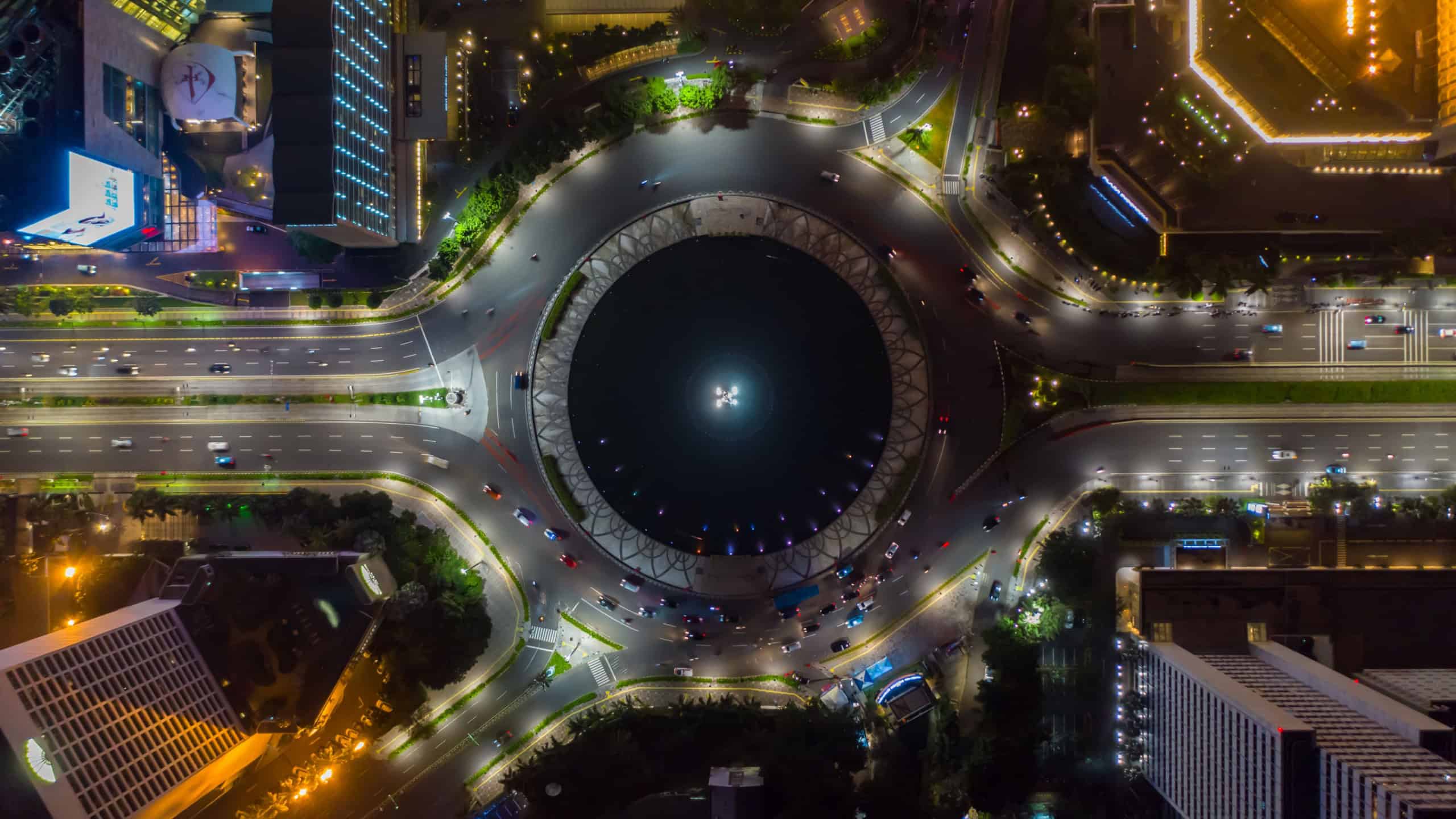 Top down overhead aerial view of moving car traffic at roundabout Vehicle road traffic around Selamat Datang monument in Jakarta, Indonesia at night in 2021