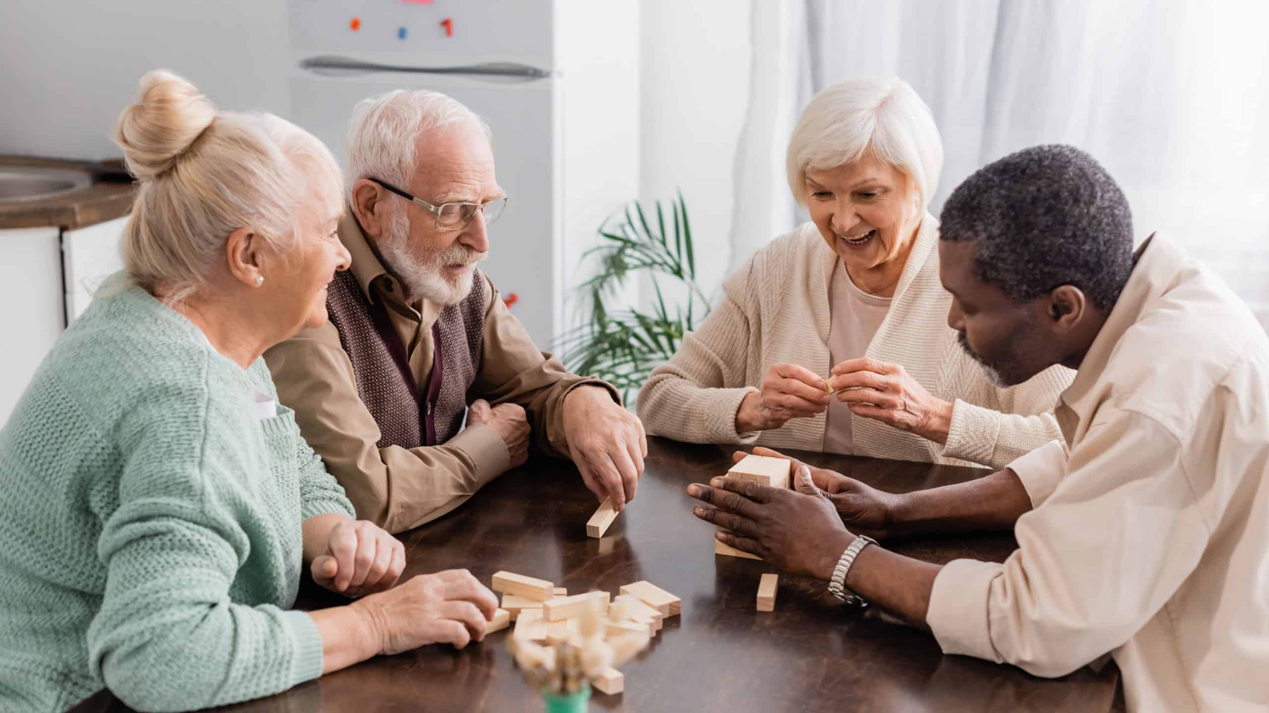 excited senior woman smiling while playing tower wood blocks game with interracial friends