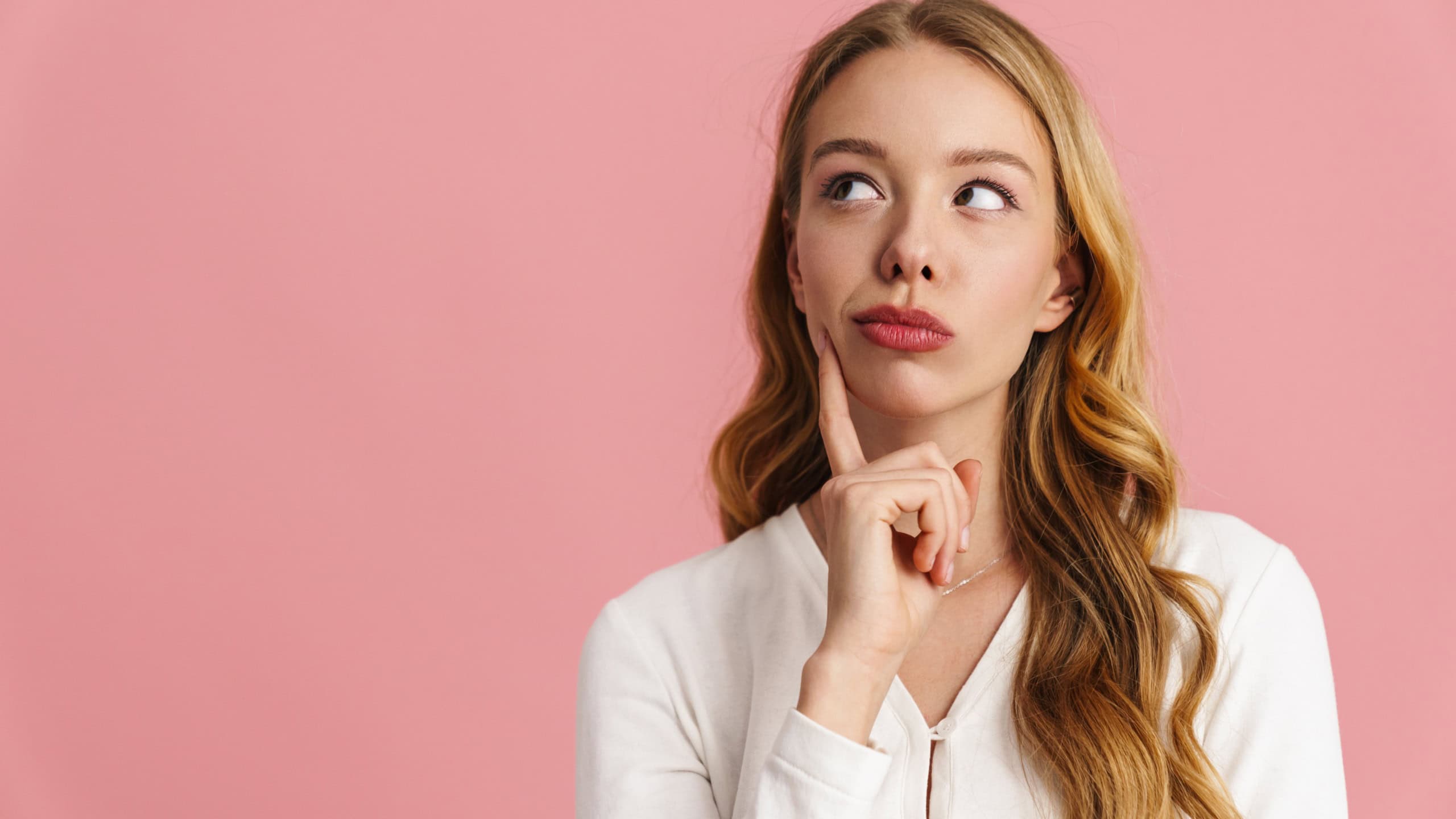 Attractive pensive young woman thinking about something isolated over pink