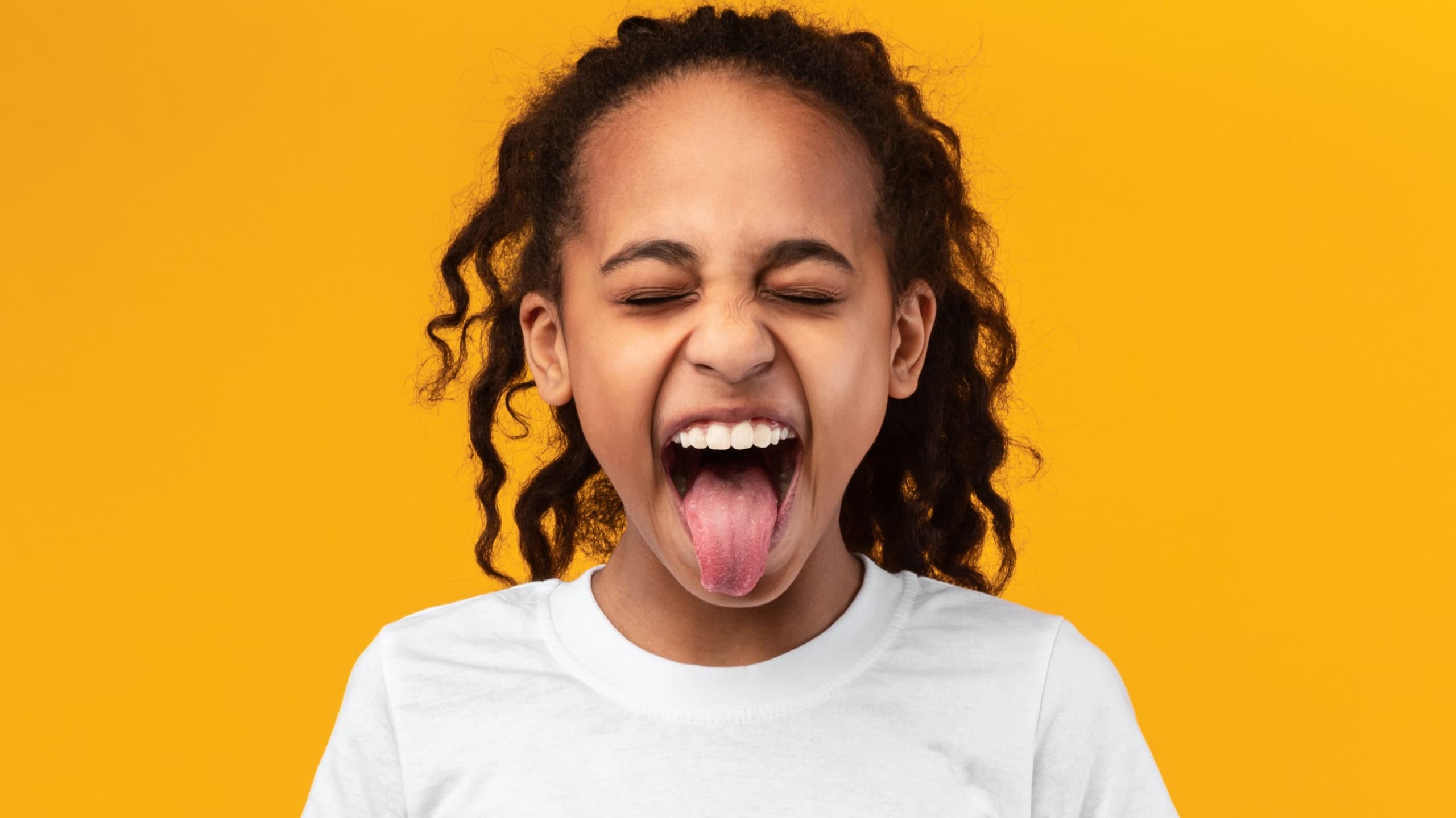 Human Emotions, Reactions And Attitude Concept. Closeup portrait of African American girl showing sticking out her tongue at camera, playing and having fun. Goofy kid fooling around
