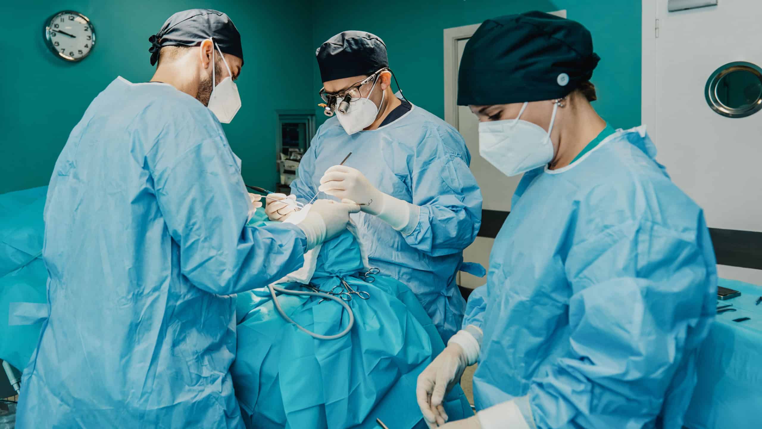 Medical doctors team operating patient in surgical room at hospital - Focus on center surgeon face