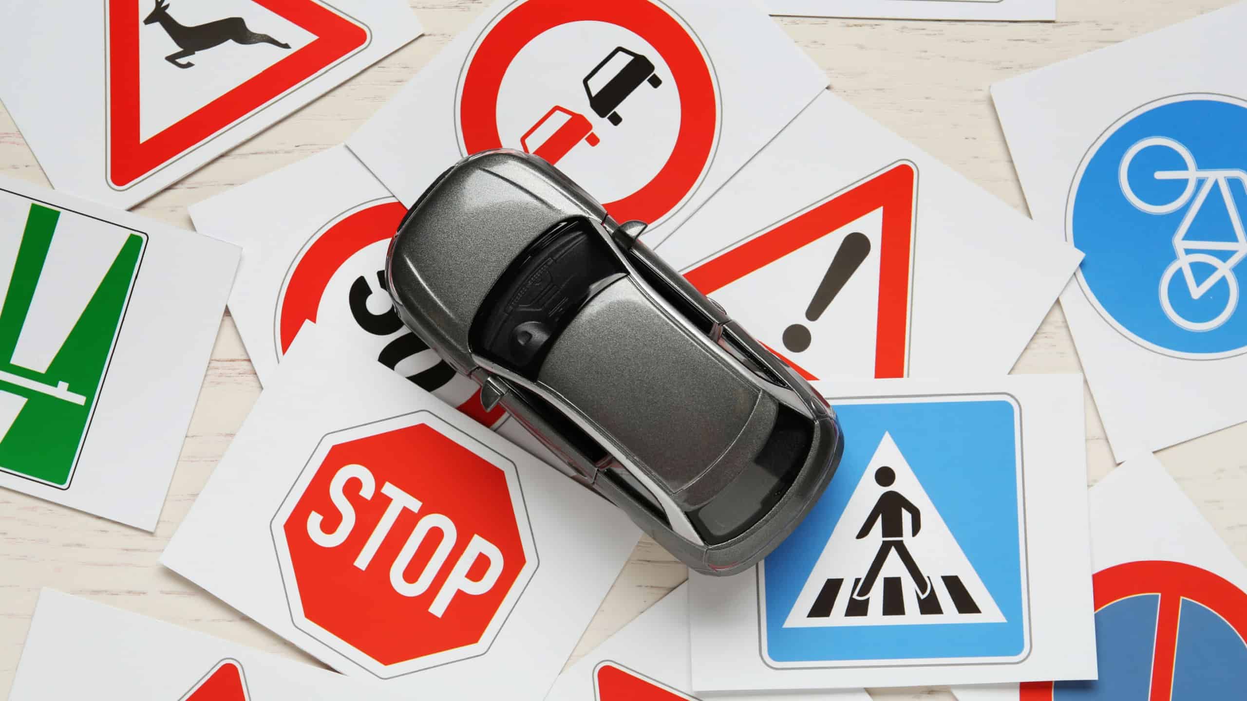 Cards with different road signs and toy car on white wooden table, flat lay. Driving school