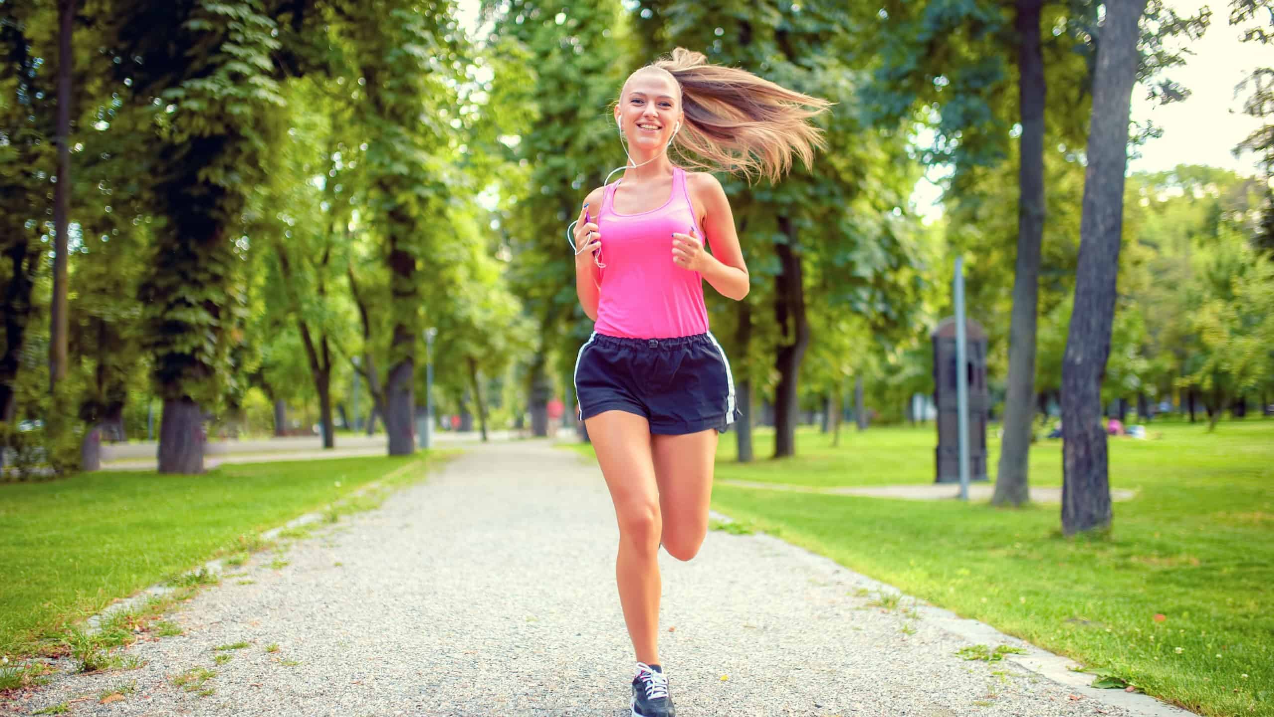 healthy and happy woman running in urban park with headphones and music
