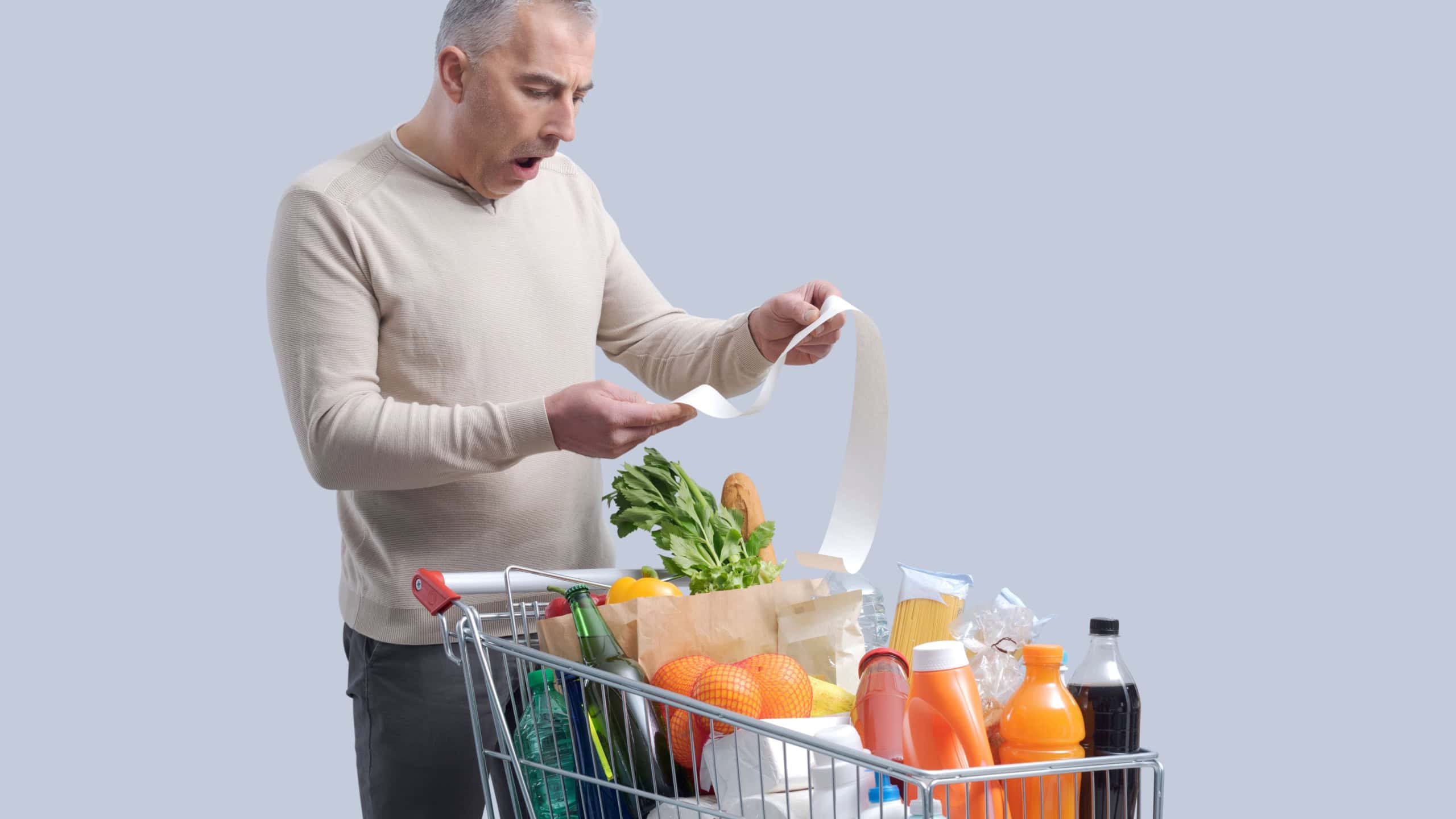 Disappointed man standing next to a full shopping cart and checking an expensive grocery bill