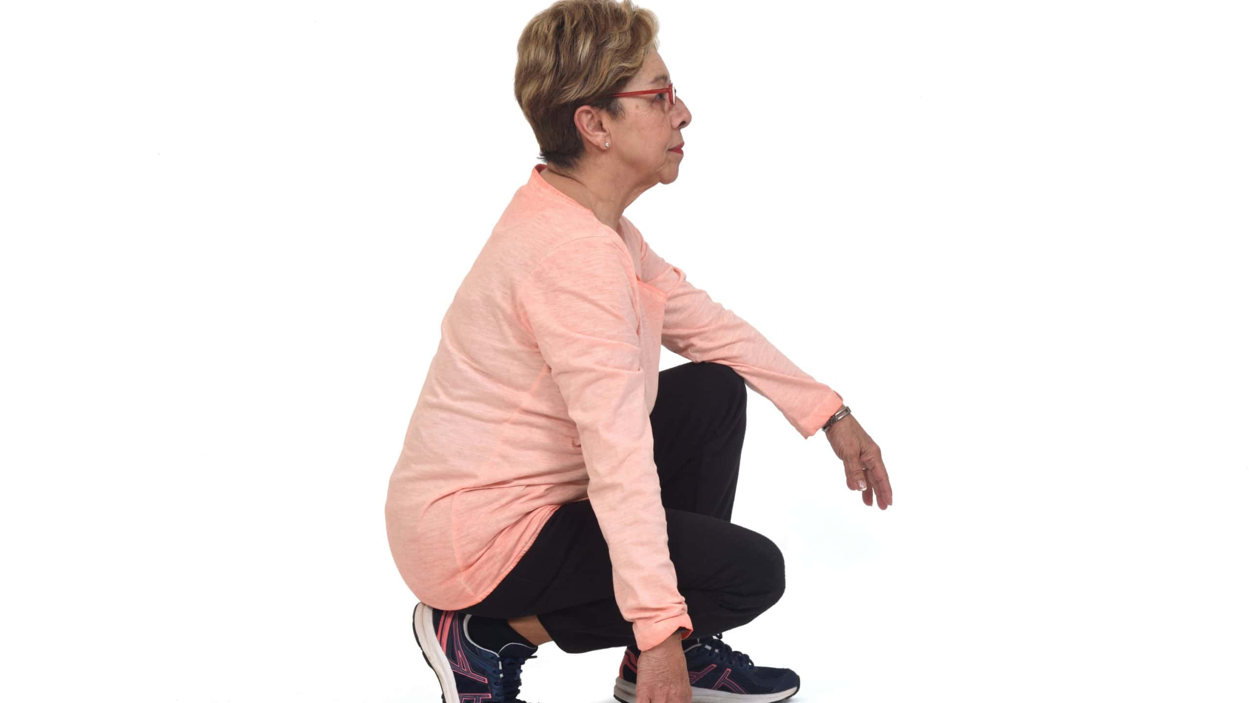 side view of aserious senior woman squatting on white backgrond