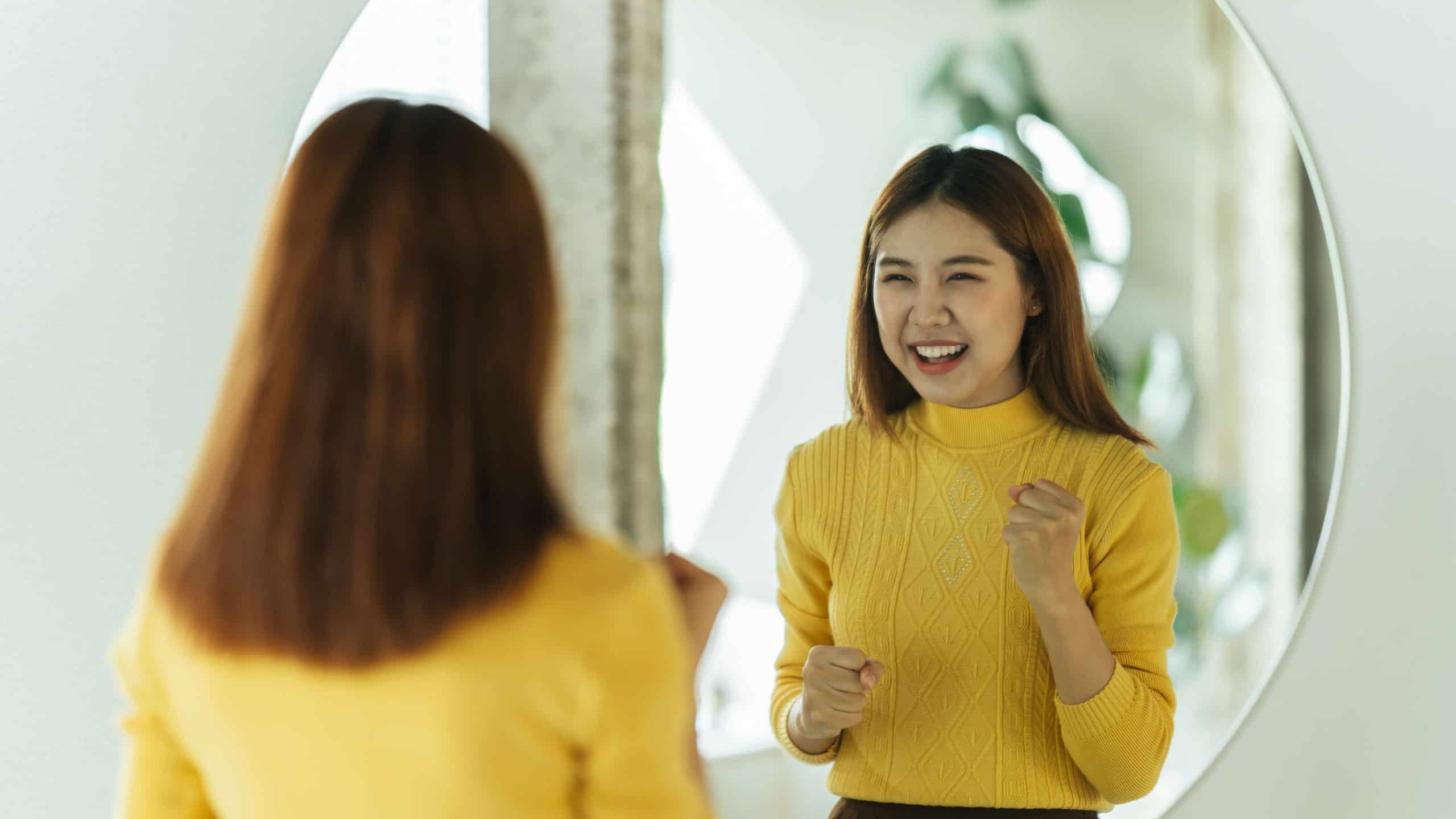 A young Asian woman talks to herself through a mirror to build her self-confidence and empower herself.
