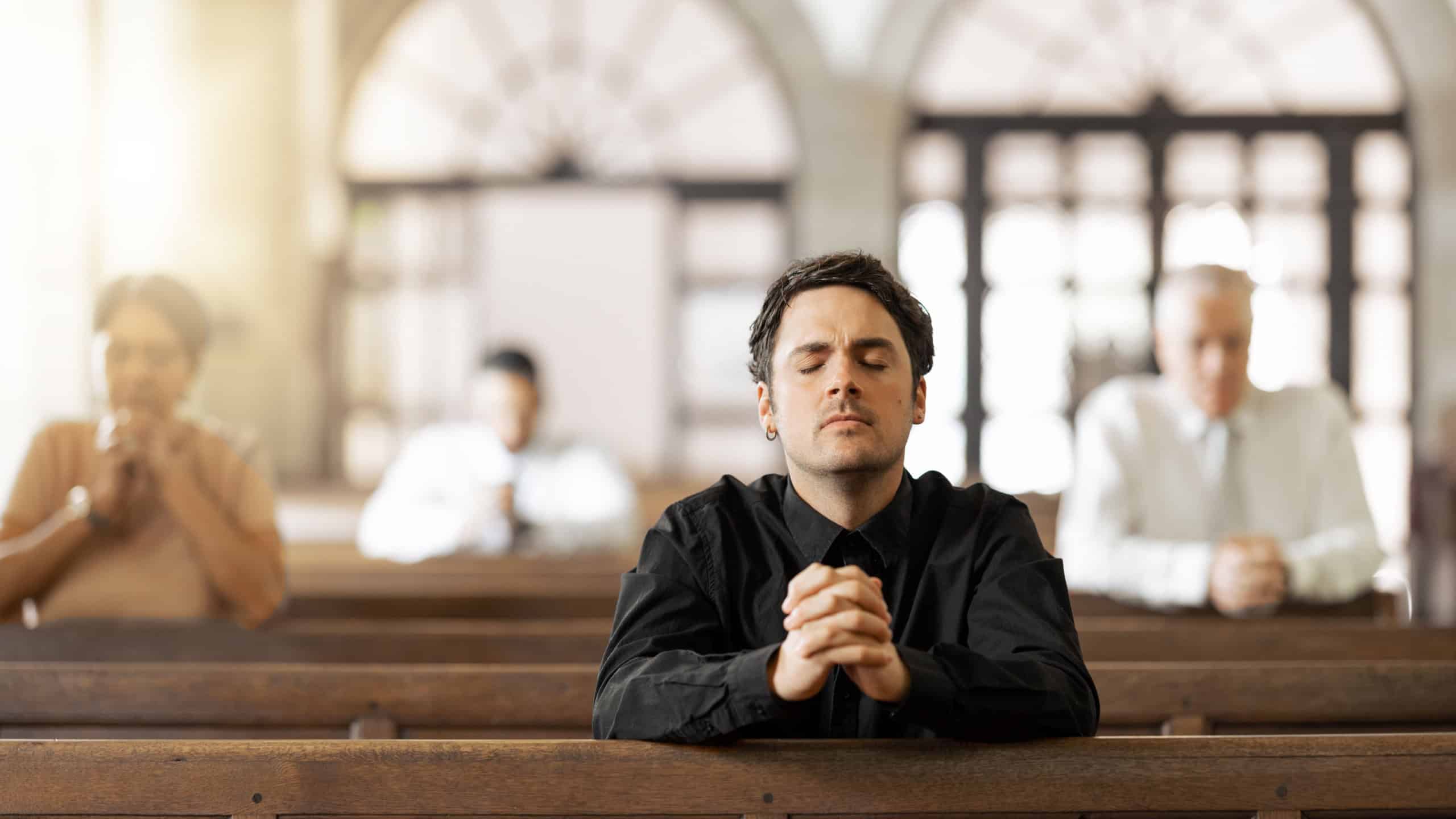 Prayer, religious and young man in church with congregation, faithful and hands together. Religion, male and worship in tabernacle for guidance, spiritual and support with closed eyes and praying