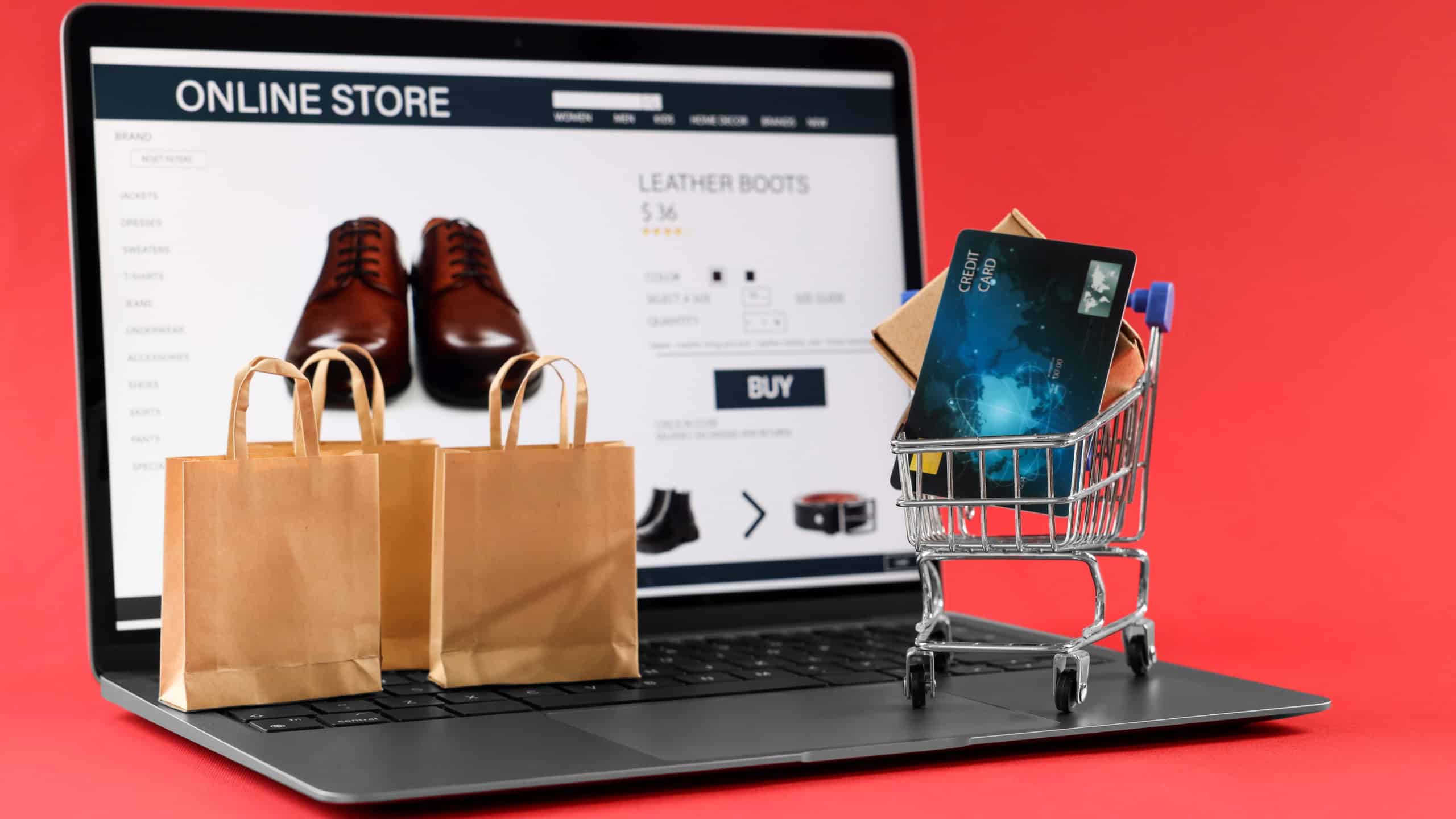 Online store. Laptop, small shopping cart, purchases and credit card on red background