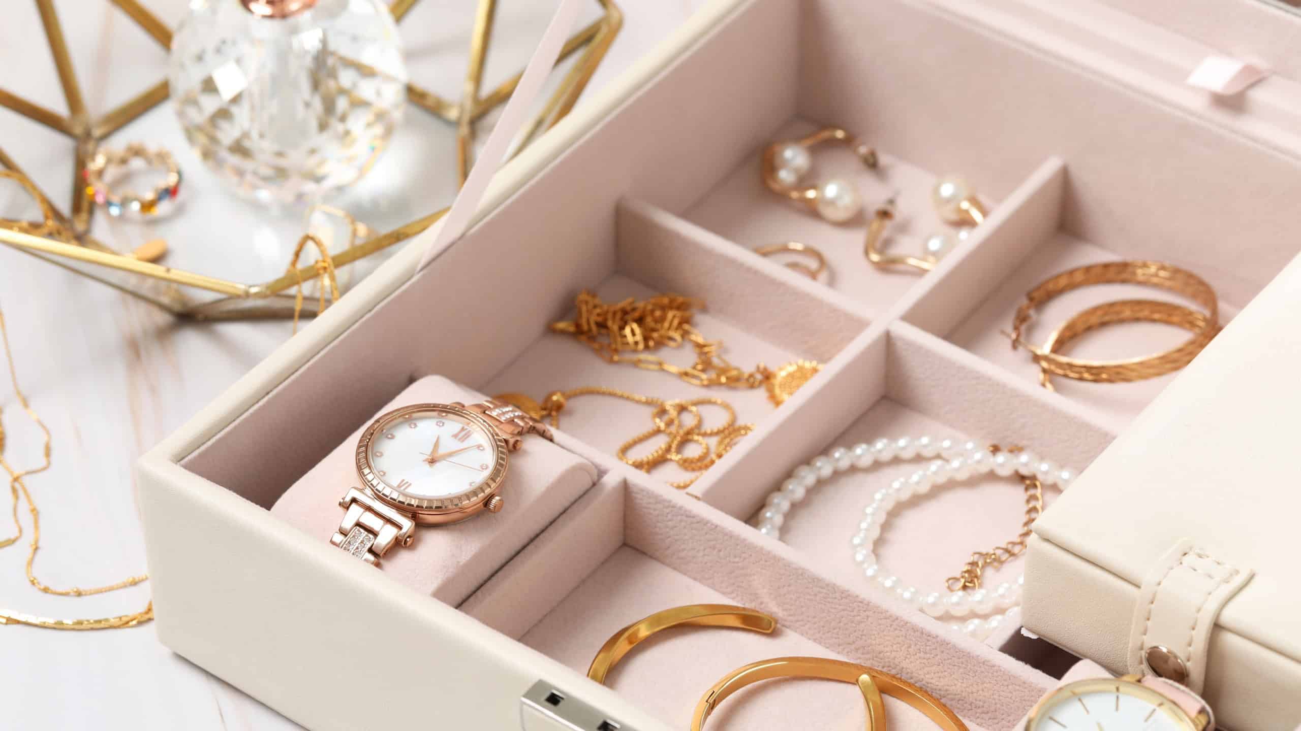 Jewelry box with many different accessories and perfume on white marble table, closeup