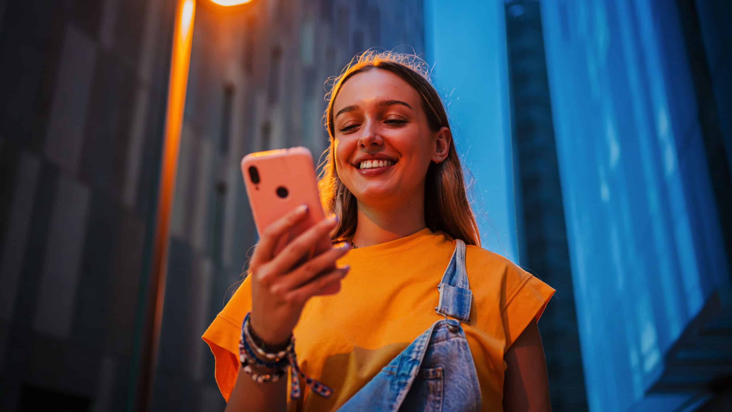 Real young adult woman using a cellphone at night. Happy female having fun with a smartphone social media app at dusk. Teenage girl browsing on internet with a mobile phone application at evening