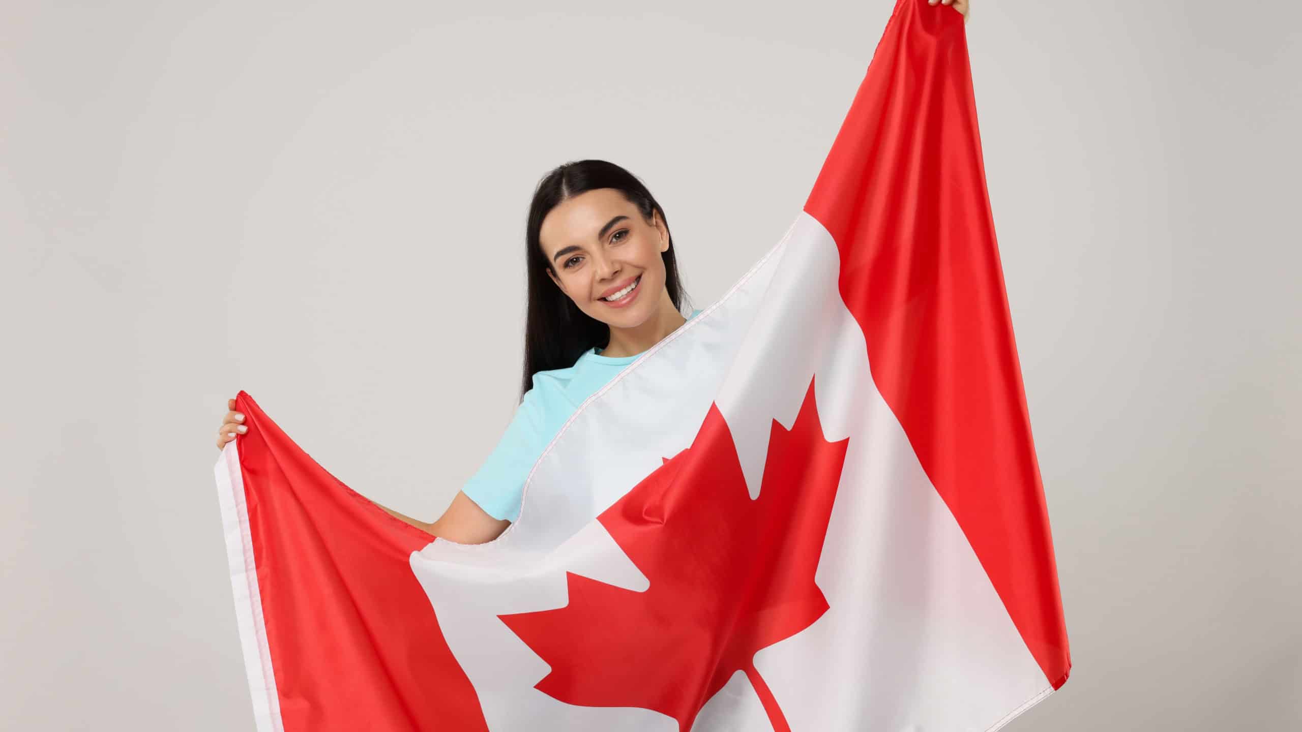 Happy young woman with flag of Canada on beige background
