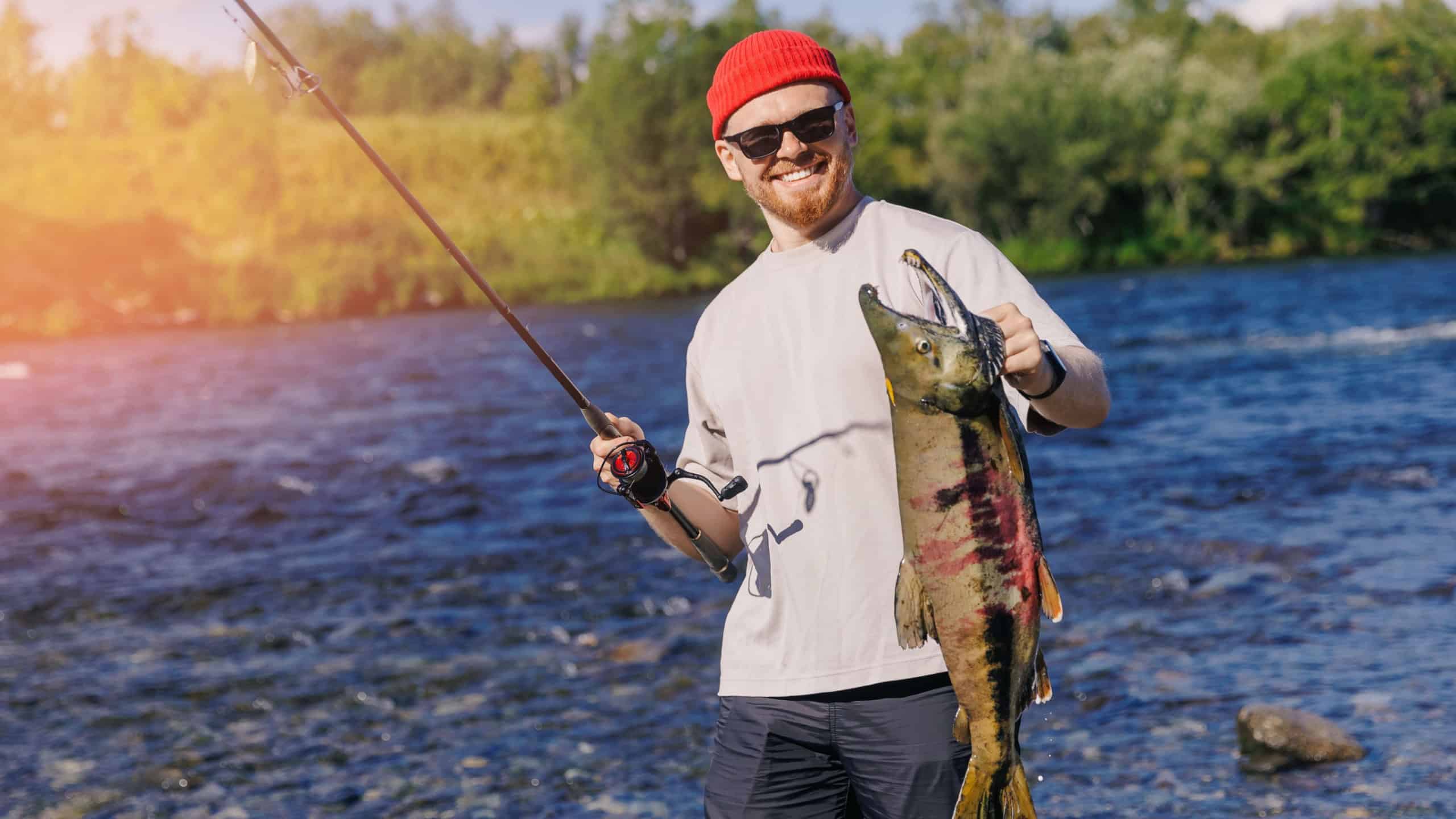 Happy man fisherman holding freshly caught big salmon fish from mountain river, concept fishing sport