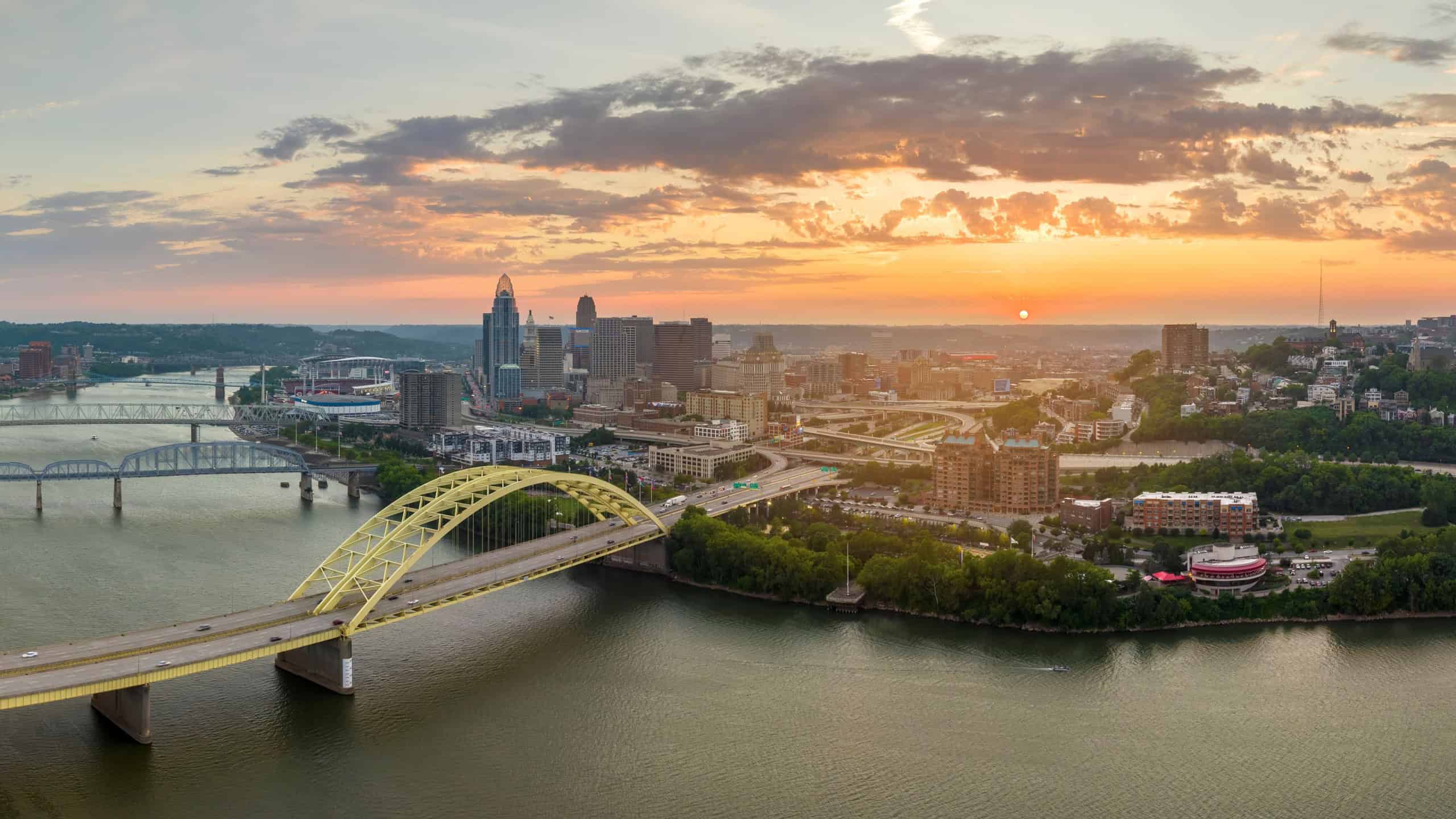 Highway traffic with driving cars on bridge in downtown district of Cincinnati city in Ohio, USA. American city skyline with brightly illuminated high commercial buildings at sunset