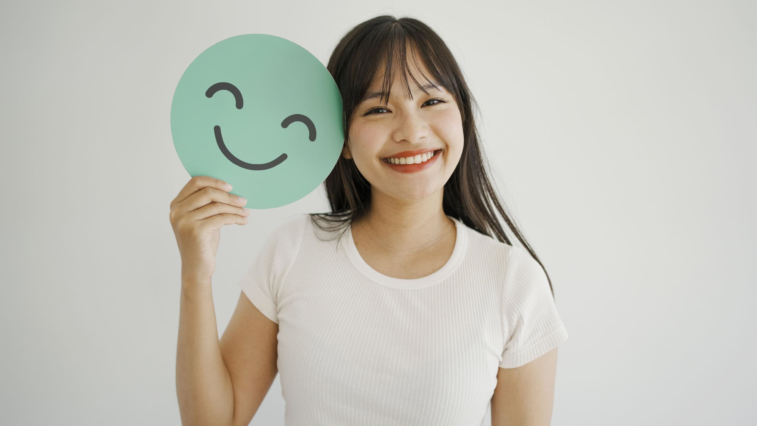 Happy young Asian woman holding smile emoji face, positive mental health, world mental health day concept