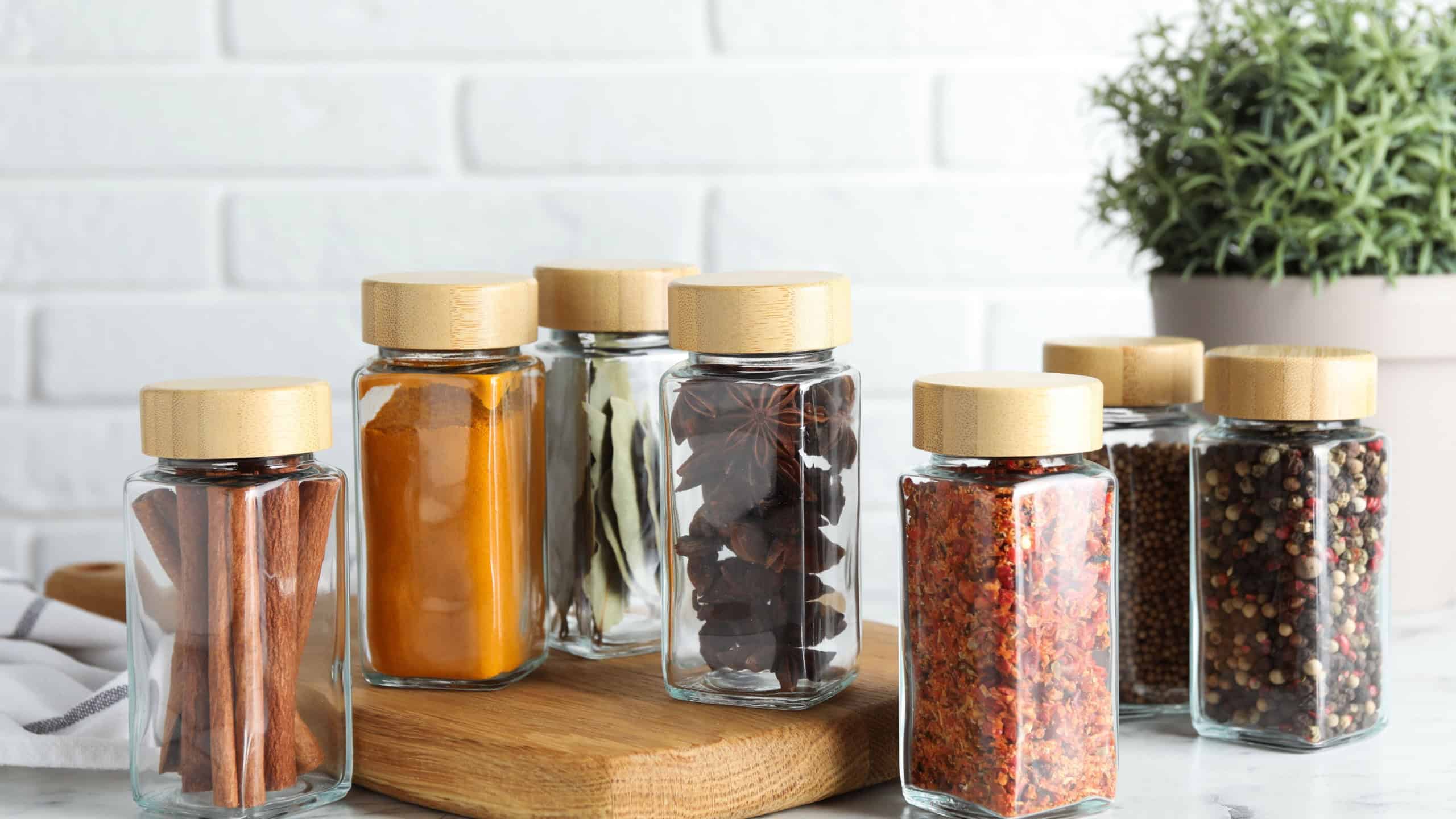 Different spices in glass jars on white marble table