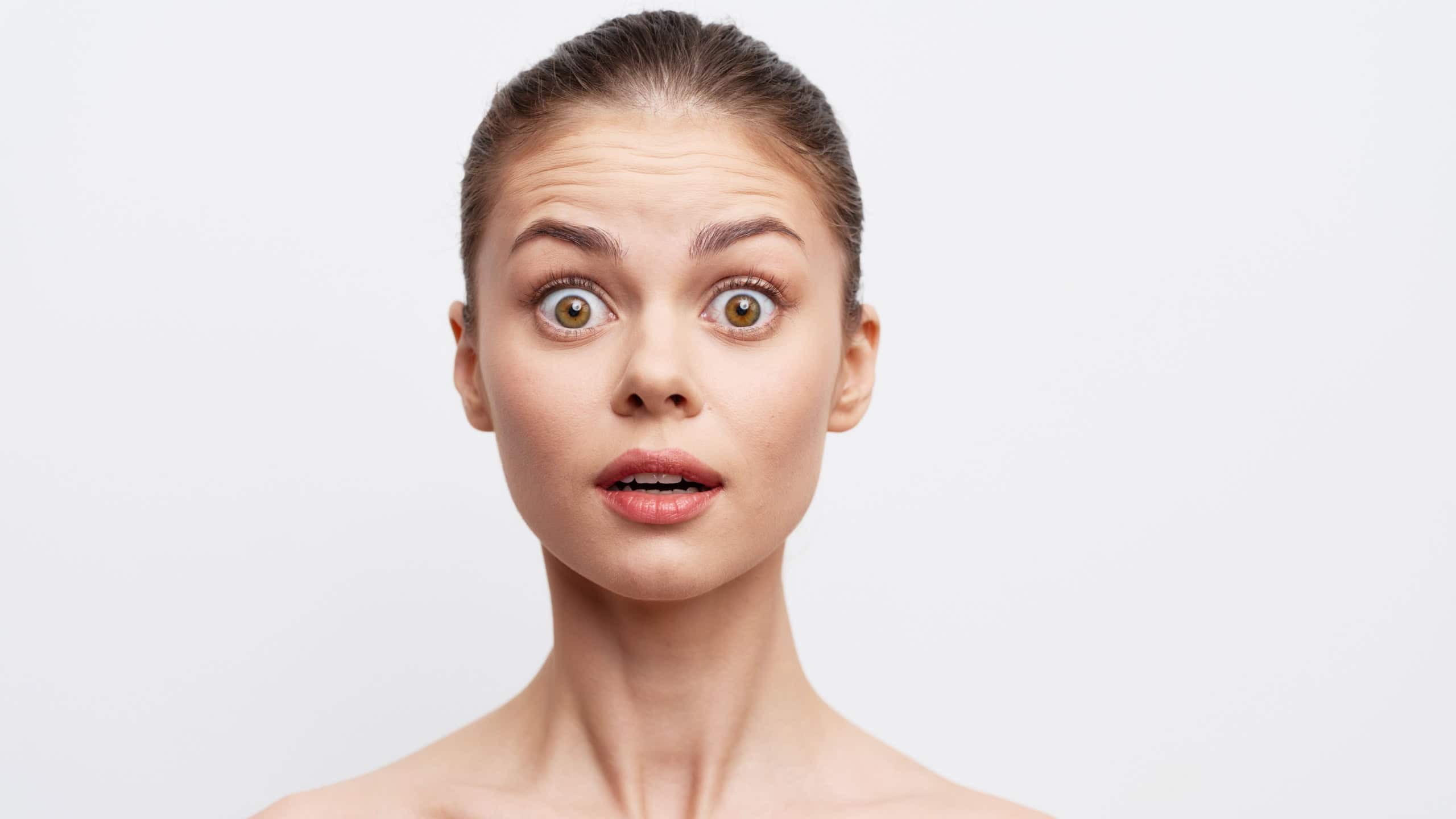 surprised young woman with wide eyes and open mouth against a plain white background, expressing shock and amazement, showcasing natural beauty and emotion clearly