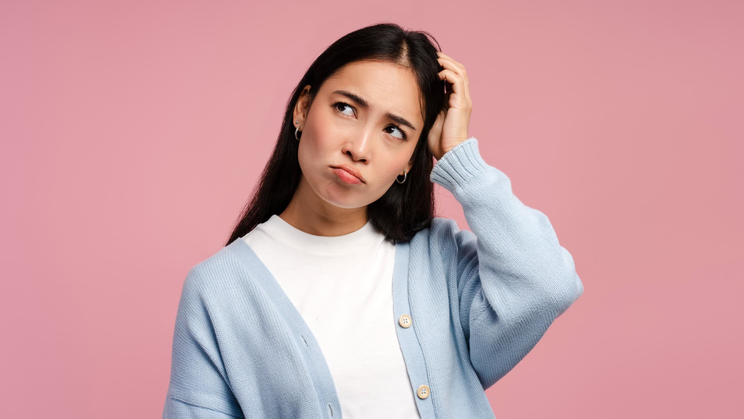 Attractive, Asian woman scratching her head feeling confused, looking away standing isolated on pink background. Shopping concept