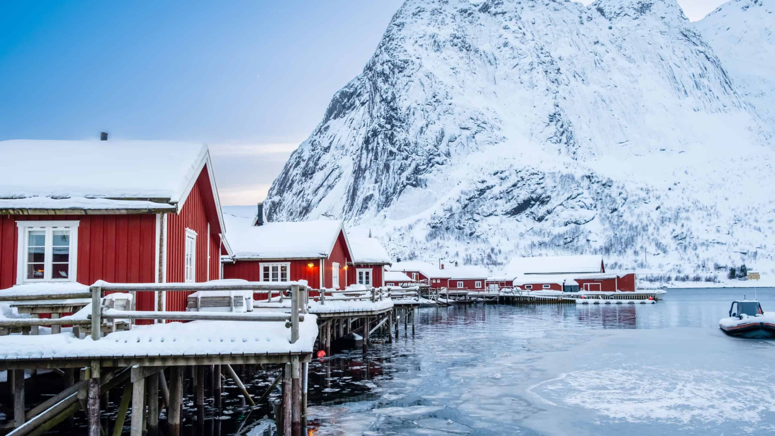 Reine village with traditional rorbu houses on Lofoten islands in winter. Scandinavian landscape with red wooden fishermen cabins on frozen sea water and snowy Reinebringen mountain, northern Norway.