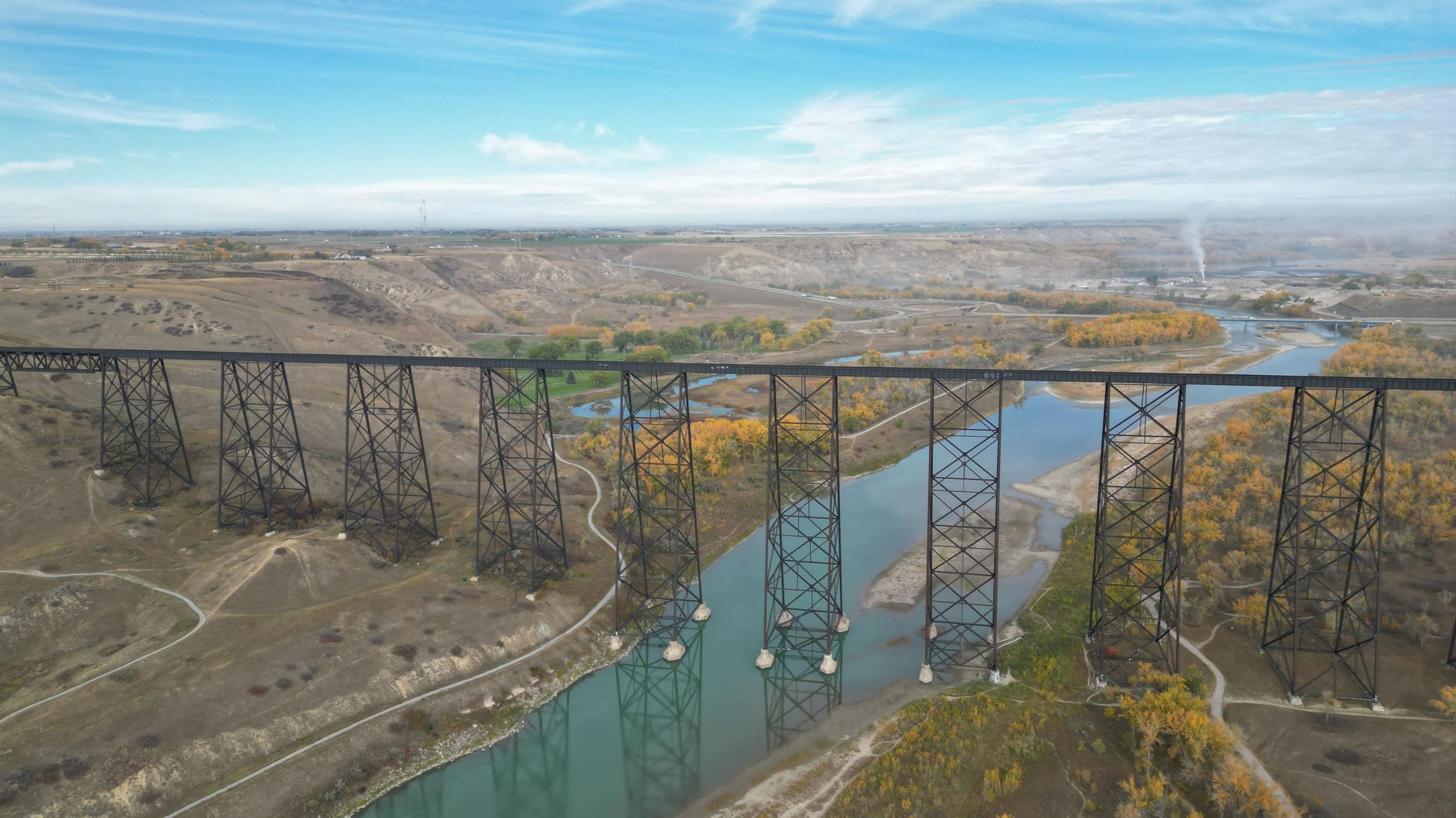 Aerial view of the High Level Bridge spanning over the Oldman River in Lethbridge, Alberta, with a scenic landscape in the background.