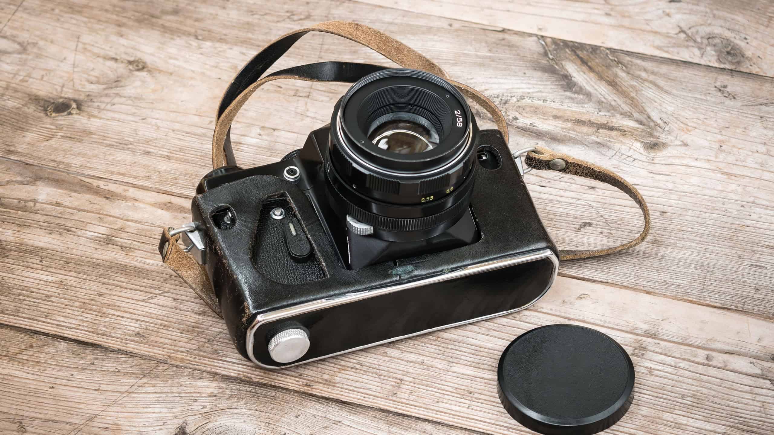 Black Soviet film camera in a leather case on a wooden unpainted surface with knots.