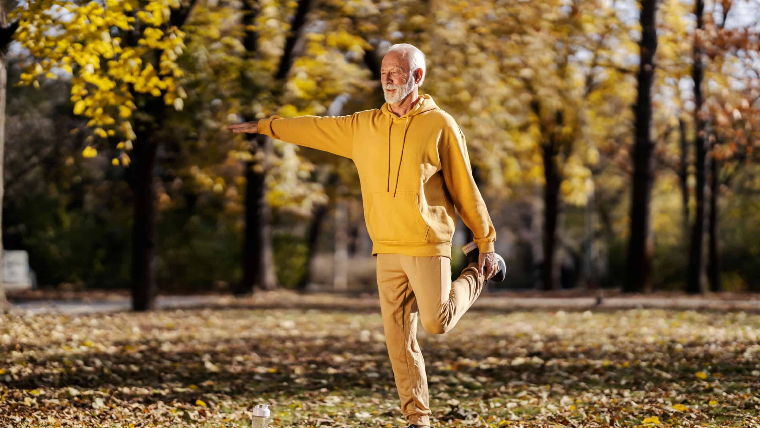 Full length of a fit old sportsman with healthy habits balancing on one foot and doing fitness exercises in nature.