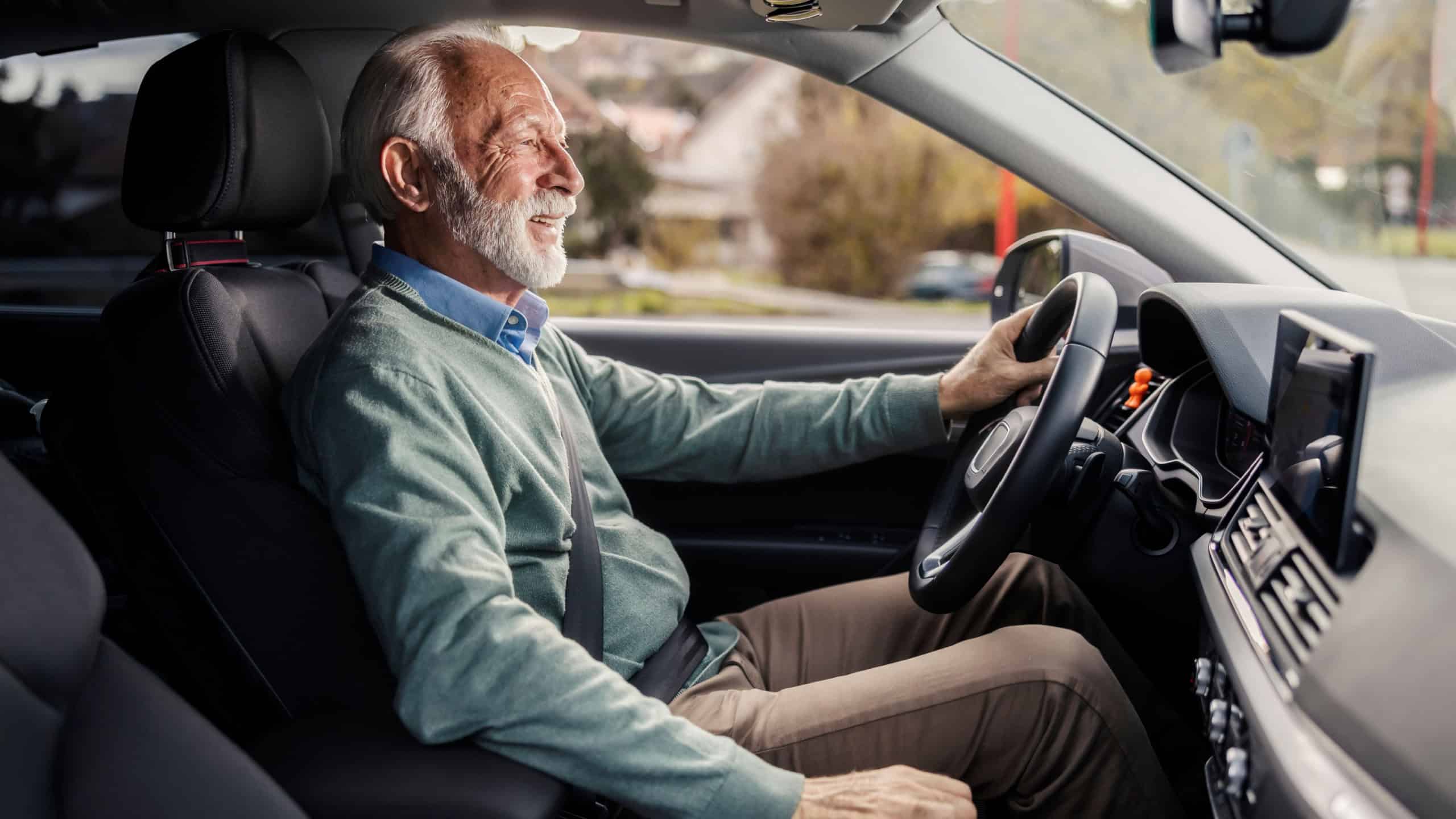 Profile view of happy senior driver sitting in his luxury car and driving on city street in traffic.