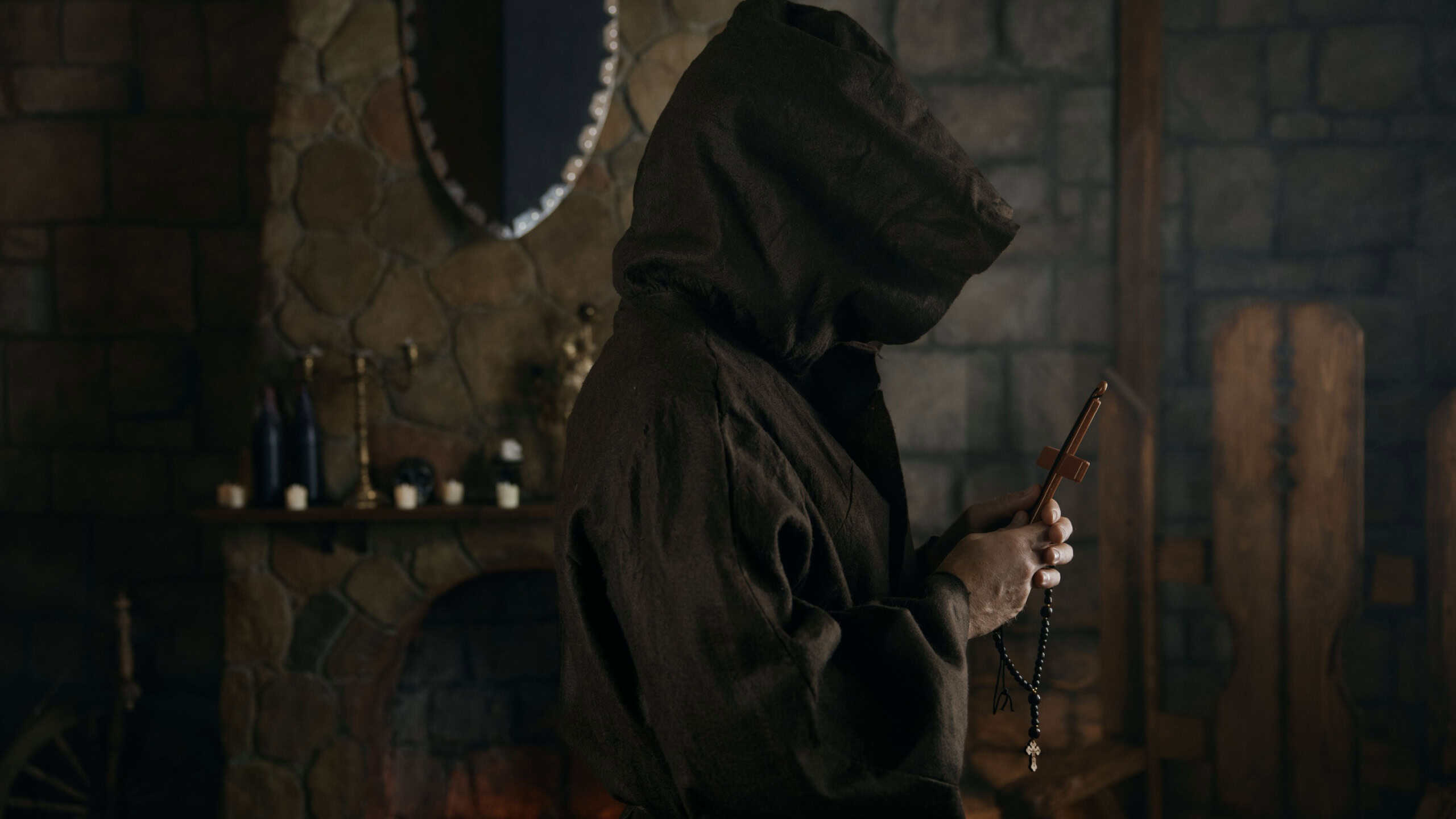 Faithful priest in robe hood praying with rosary beads and cross