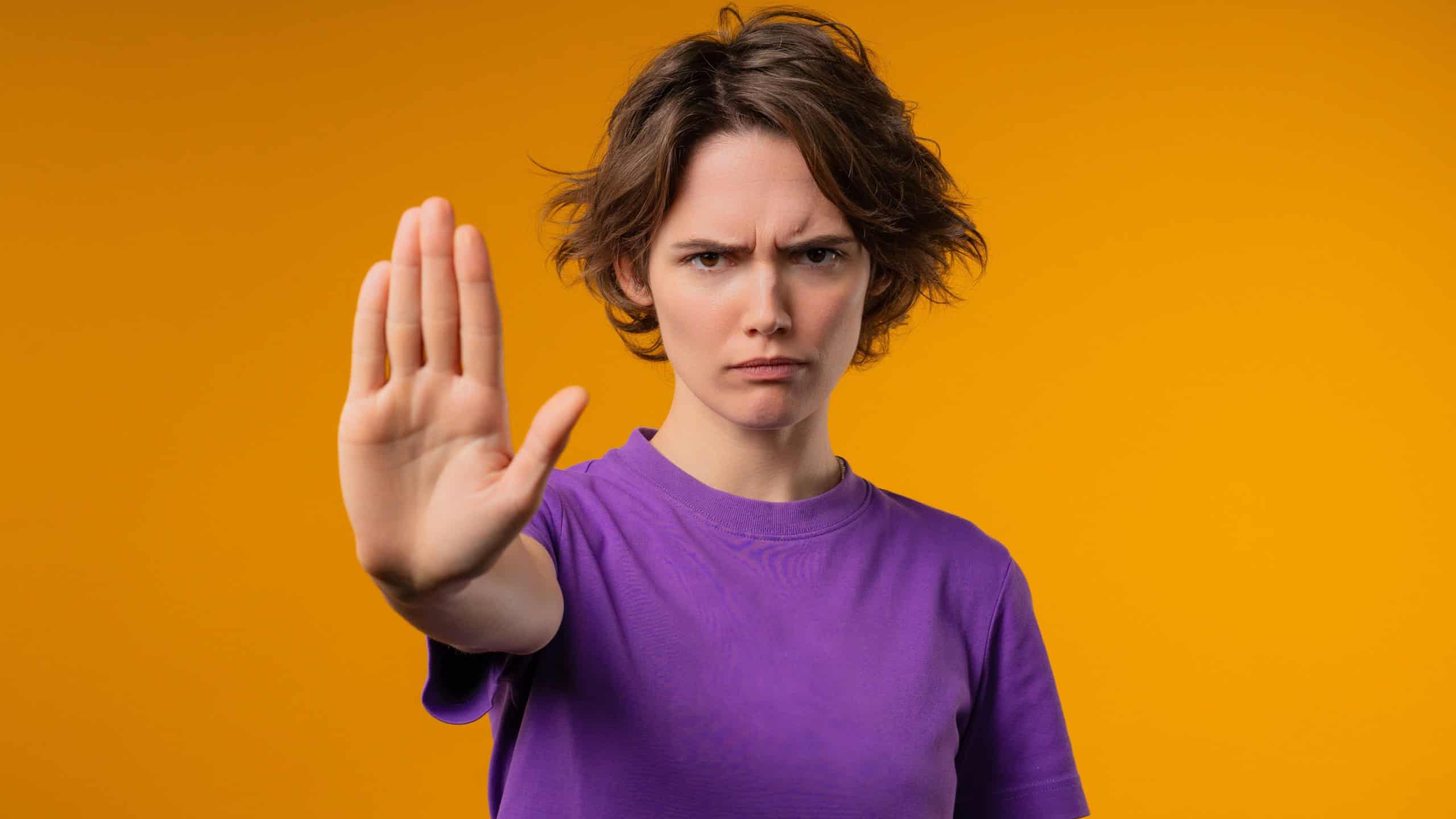 Uninterested stylish young woman disapproving with stop sign. Dont play with me, enough. Portrait of lady on yellow background. High quality