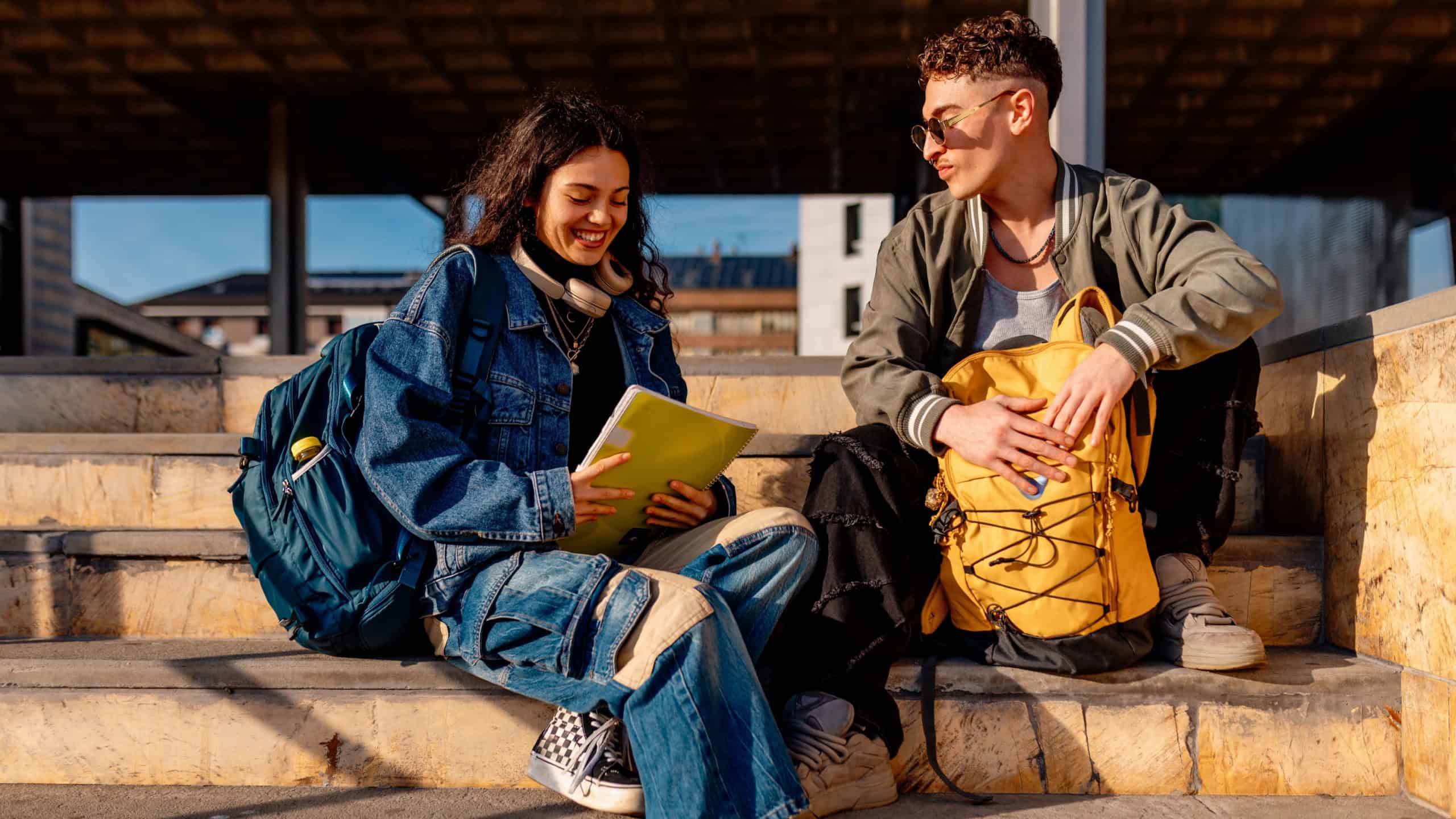 Two multiracial college students are sitting on university steps, studying and talking