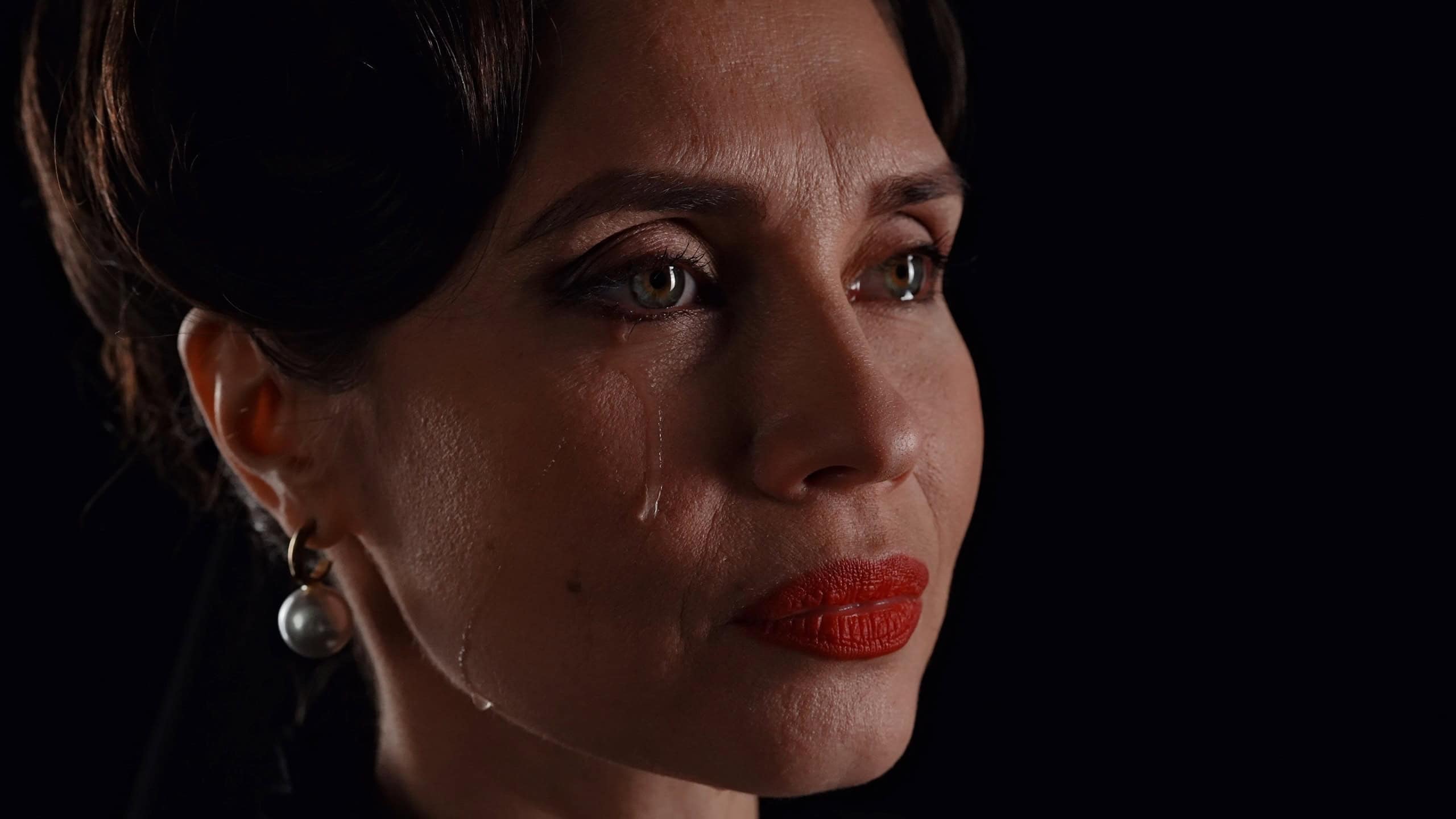 Woman actress in retro outfit with pin-up hairstyle and makeup posing at camera isolated on black background, posing looking away and crying, tears flowing on the cheek.