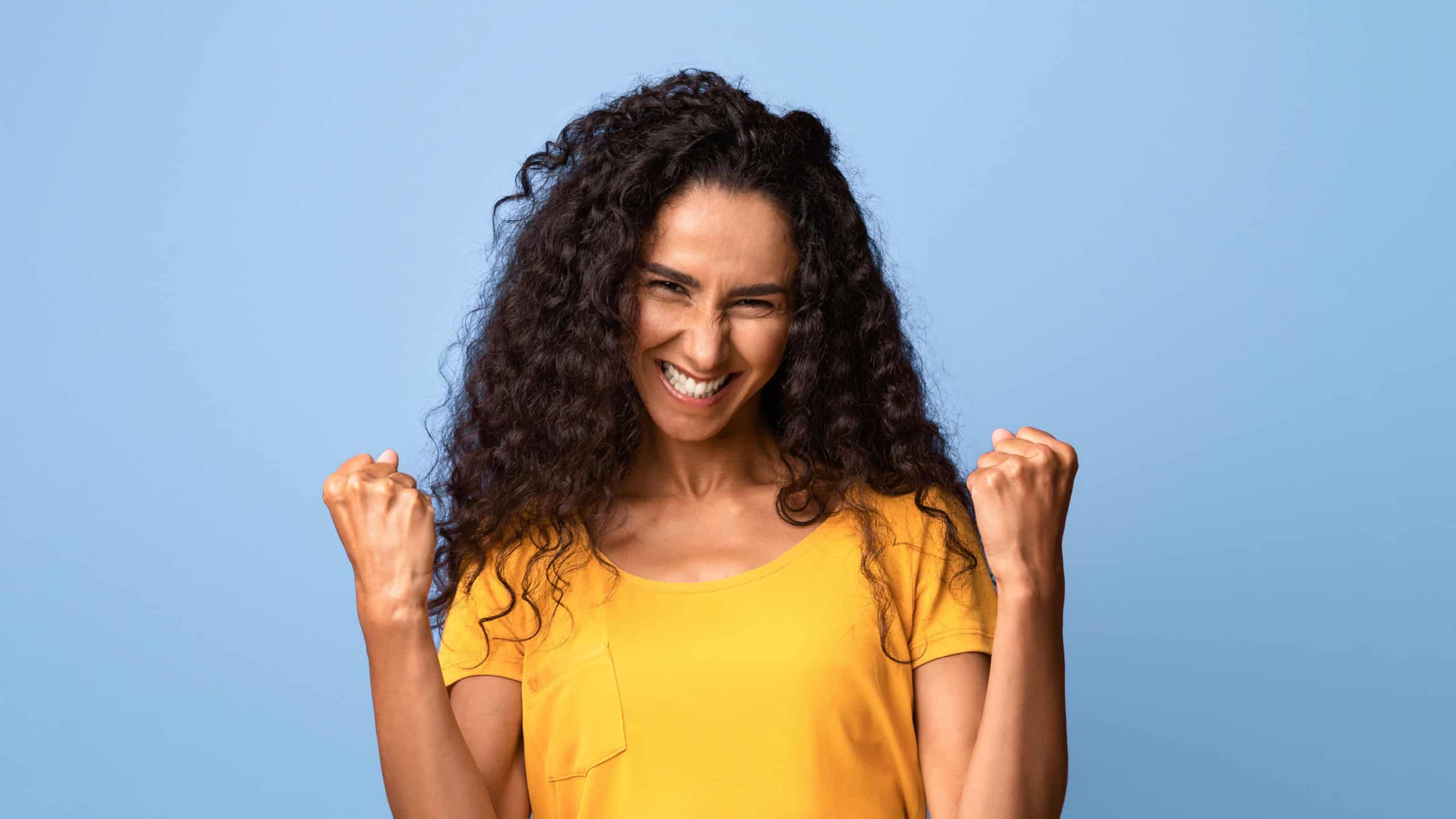 Joy Of Success. Euphoric Young Brunette Woman Celebrating Victory With Clenched Fists Over Purple Studio Background, Raising Hands, Excited Lady Cheering Luck, Portrait Of Happy Winner, Copy Space