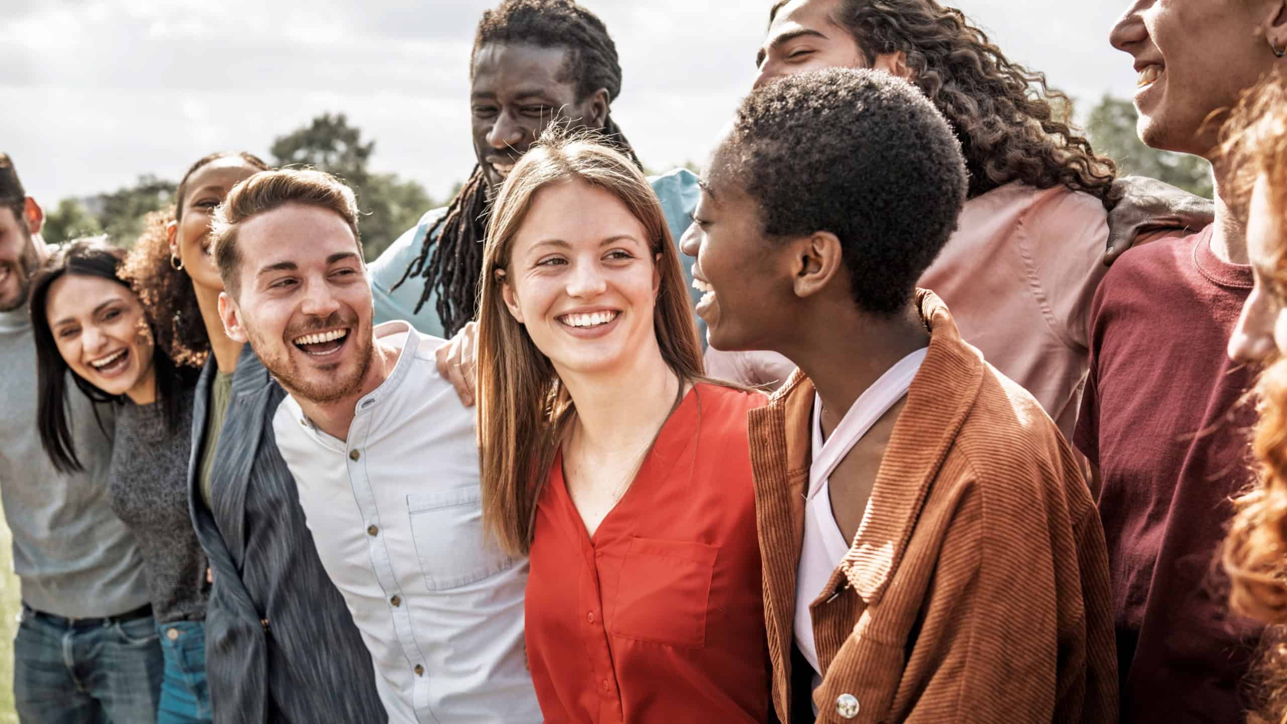 Diverse group of young friends enjoying time together outdoors, laughing and smiling in a warm and supportive atmosphere. Concept of friendship, inclusion, youth and multicultural community.